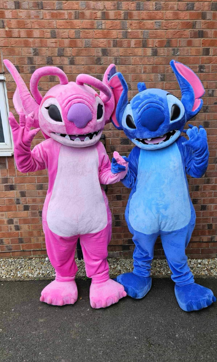 Two mascots , angel and stitch , are standing next to each other in front of a brick wall.