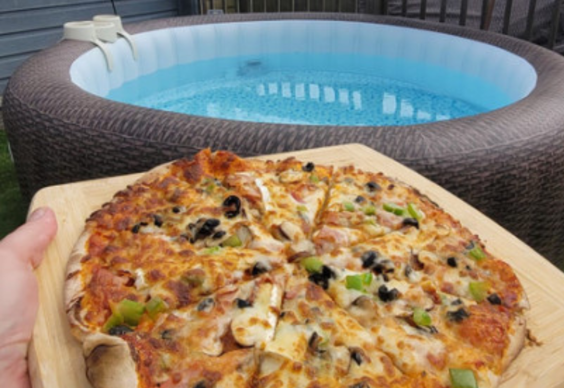A person is holding a pizza in front of a hot tub.