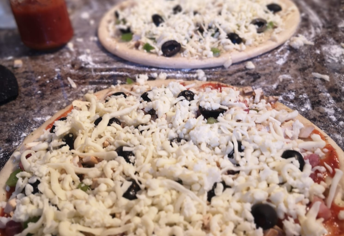 Two pizzas are sitting on a table with cheese and olives on them