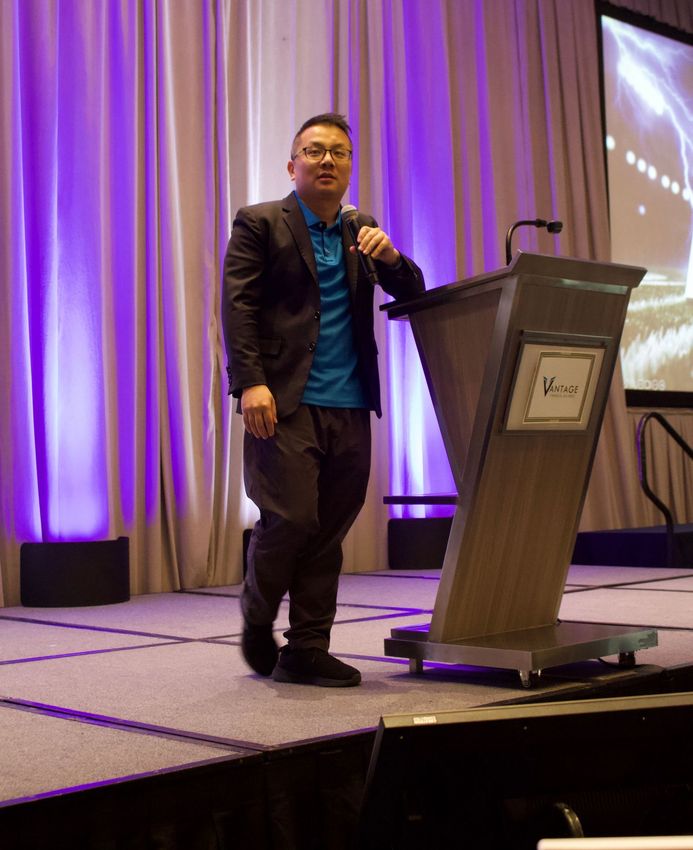 A man in a suit stands at a podium holding a microphone