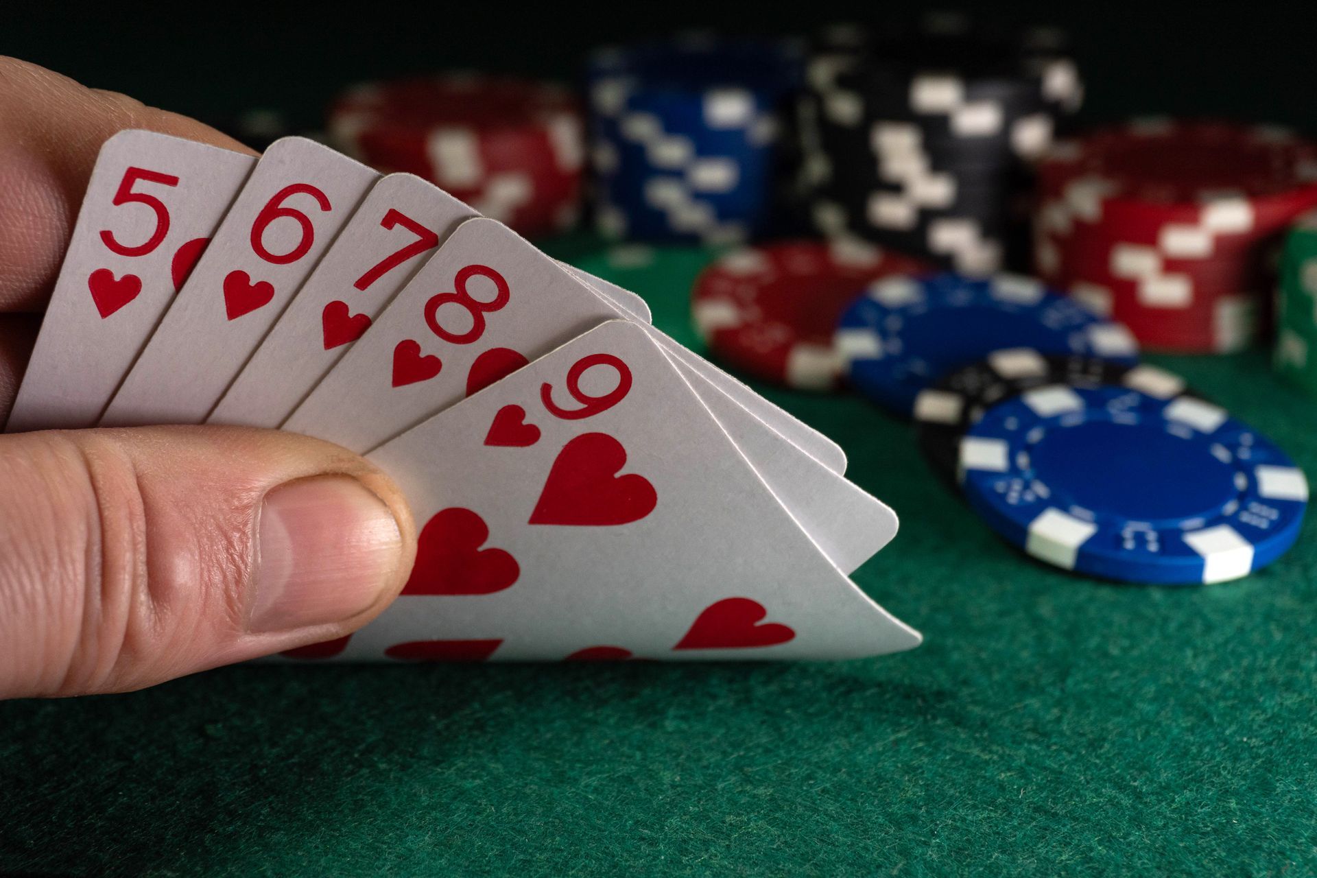 A man holds playing cards with hearts or a straight flush in his hand. 