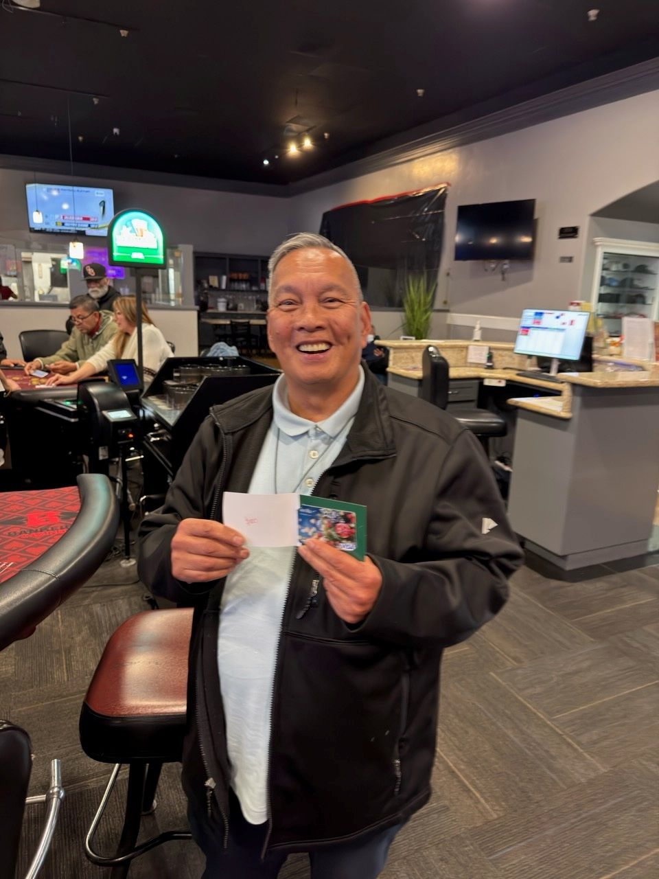 Man smiling, holding a ticket, in a casino setting.
