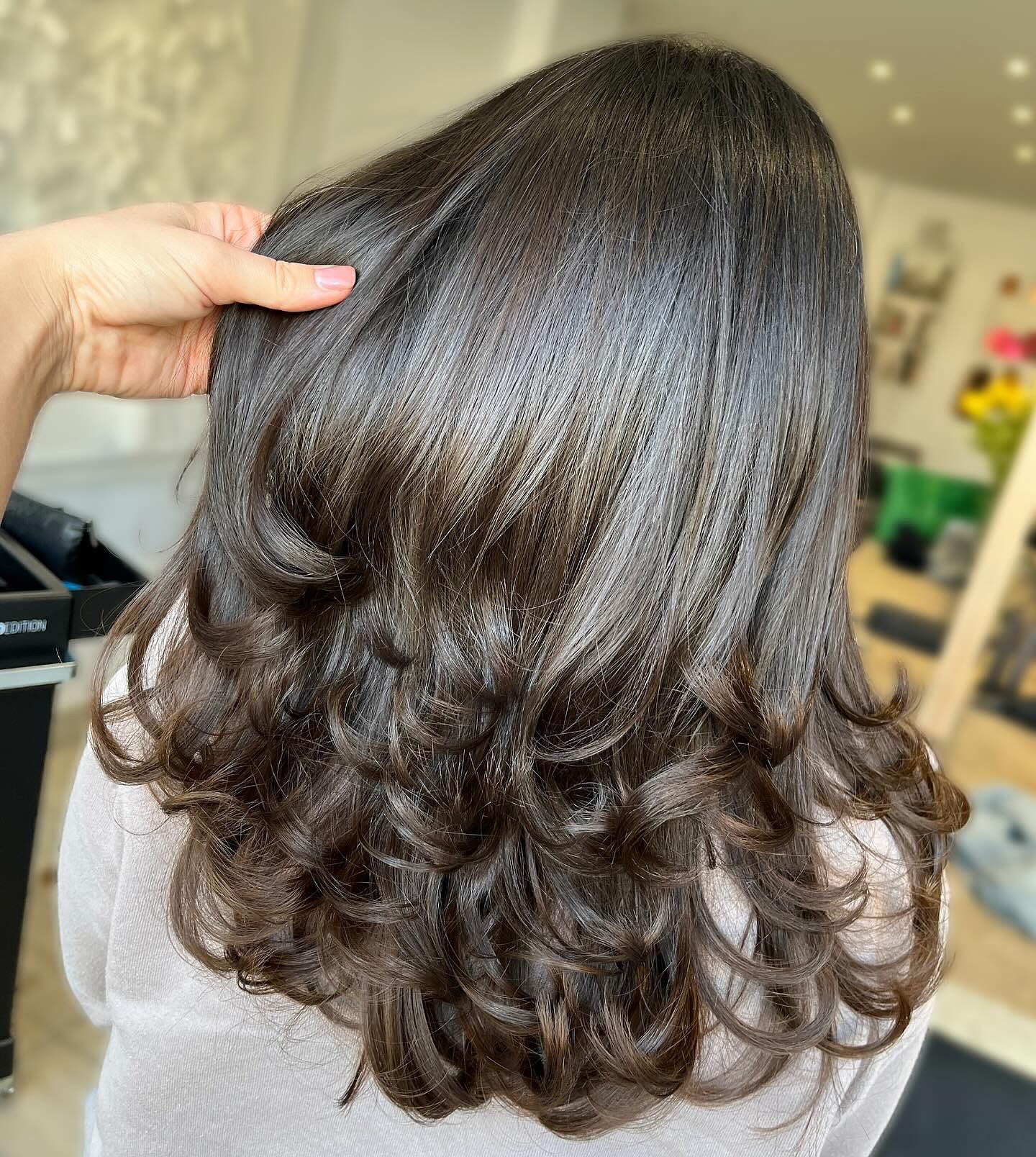 Dark brown wavy hair, styled with loose curls, hand touching the hair.