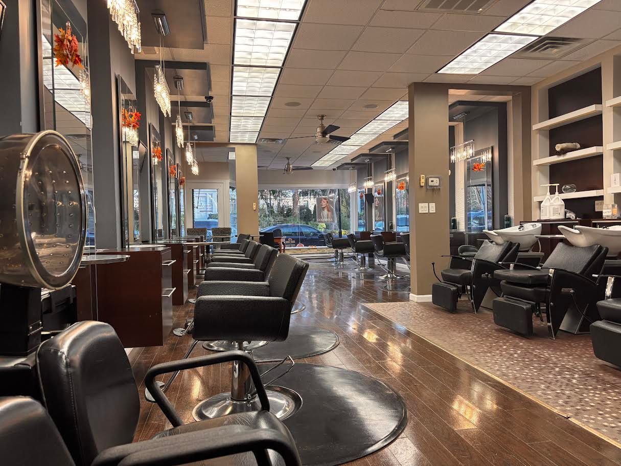Hair salon interior with styling stations and chairs. Rows of mirrors, overhead lights, and a patterned floor.
