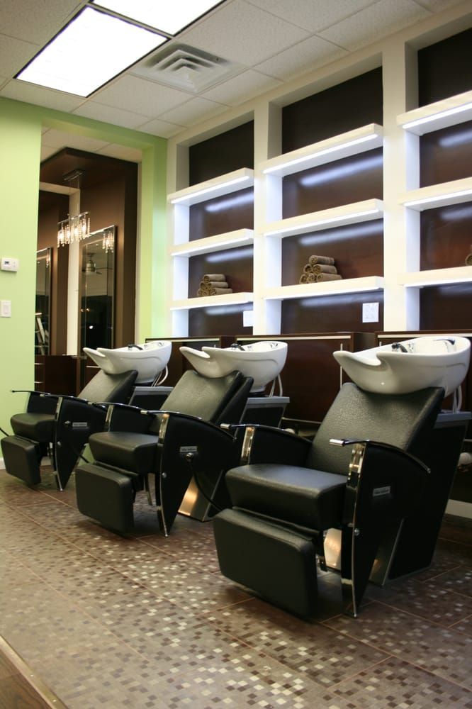 Salon interior with three black wash chairs, white sinks, and built-in shelves with products.