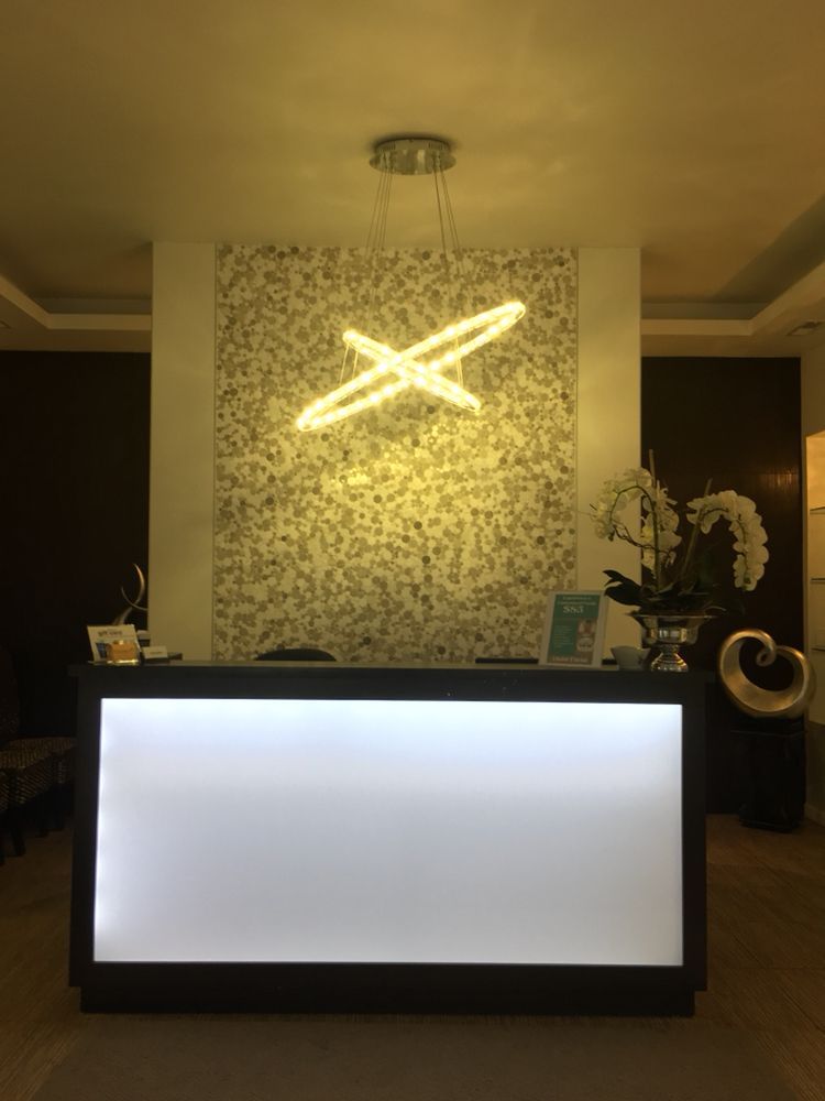 Reception desk with glowing front, illuminated logo, mosaic wall, and overhead light.