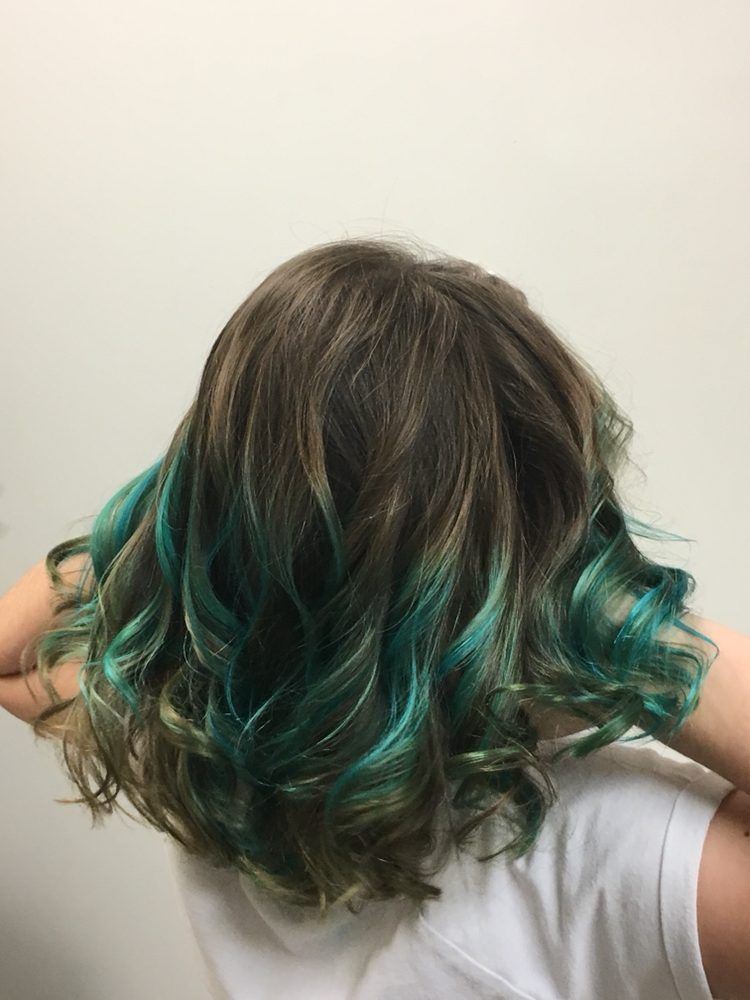 Woman's hair, brown at the roots with teal green tips, styled in loose curls.