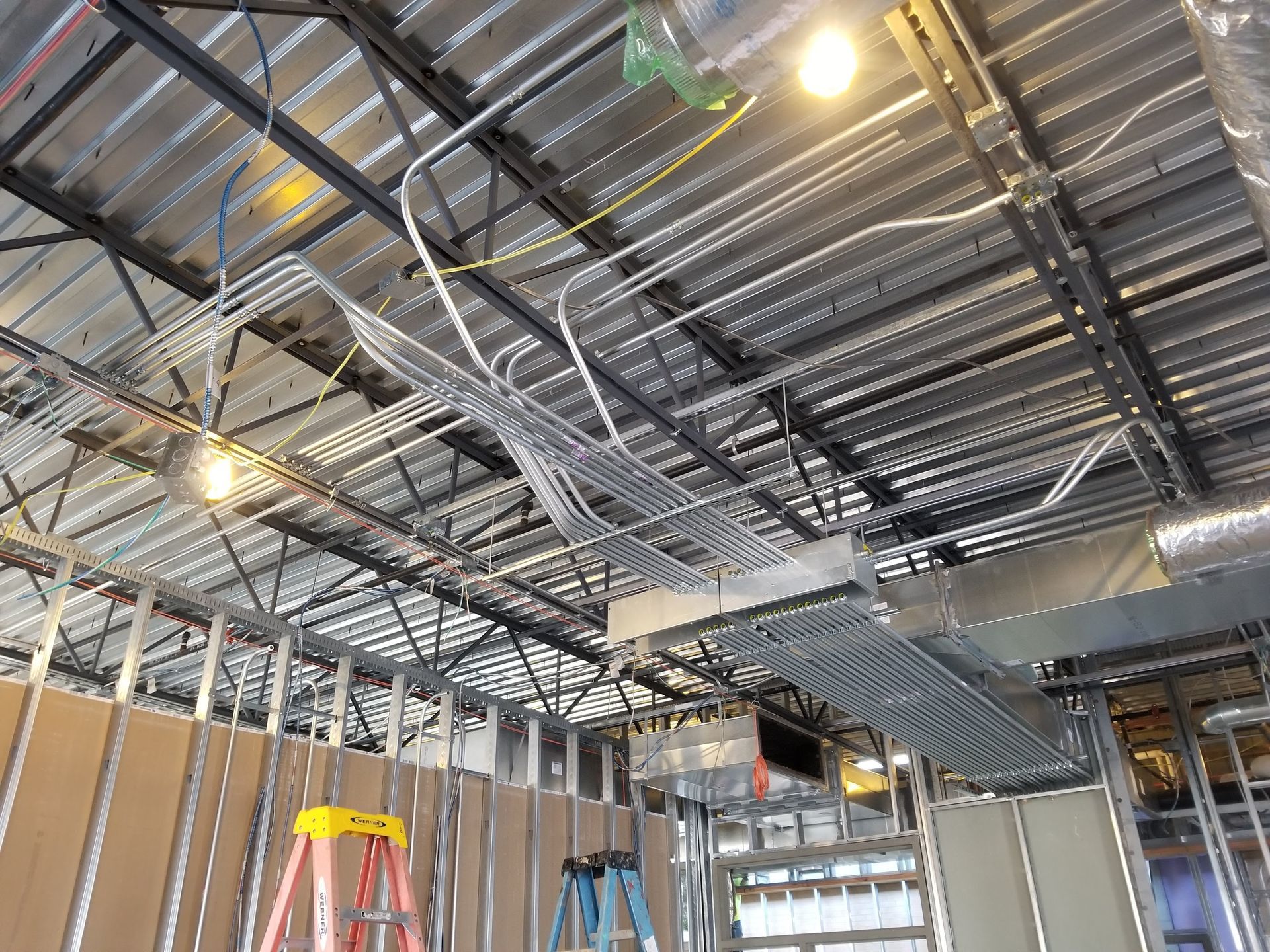 Construction site with exposed metal studs, ductwork, and electrical conduit on a corrugated metal ceiling.