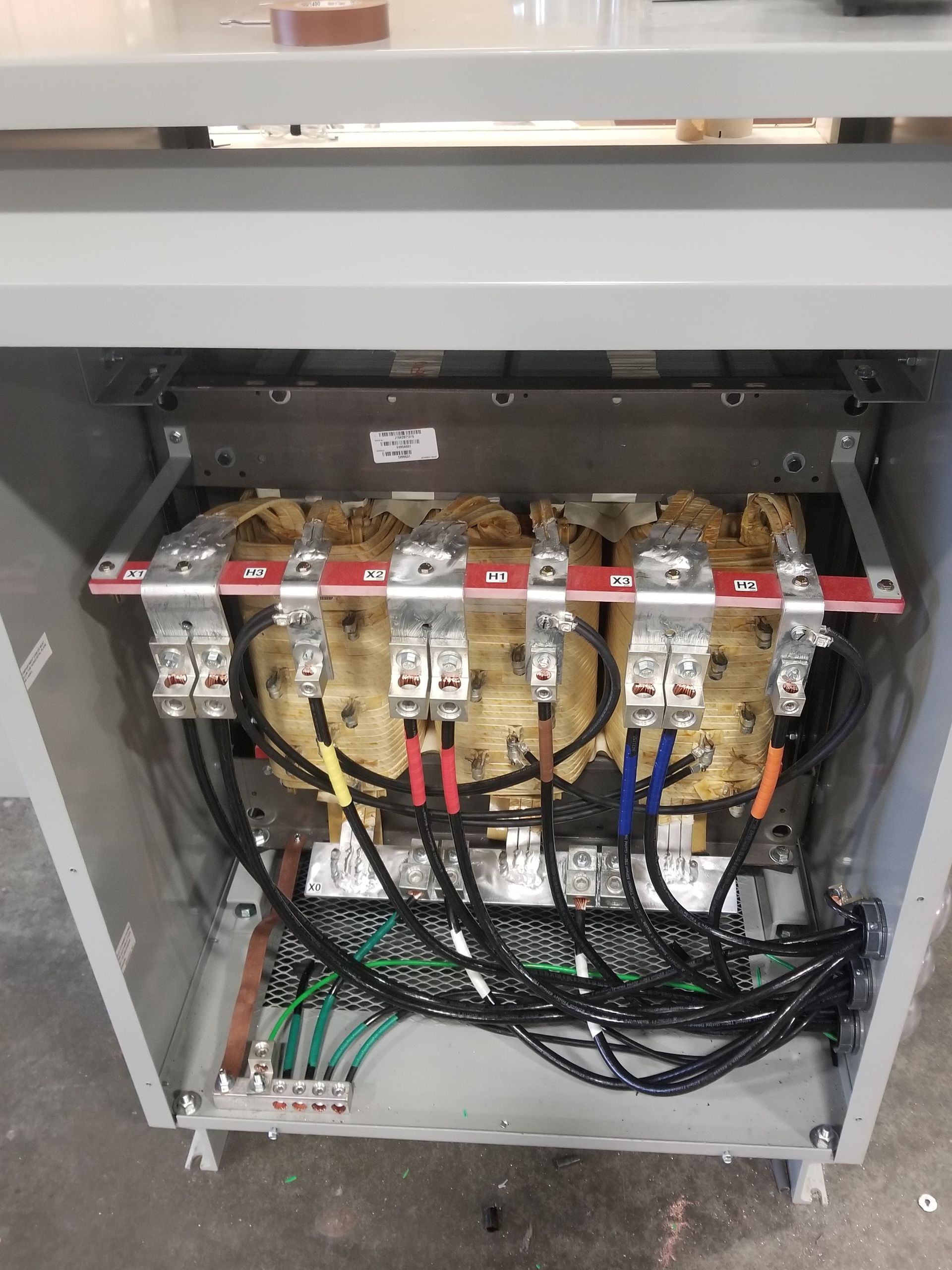 Electrical transformer in a metal cabinet, with wiring and bus bars visible.