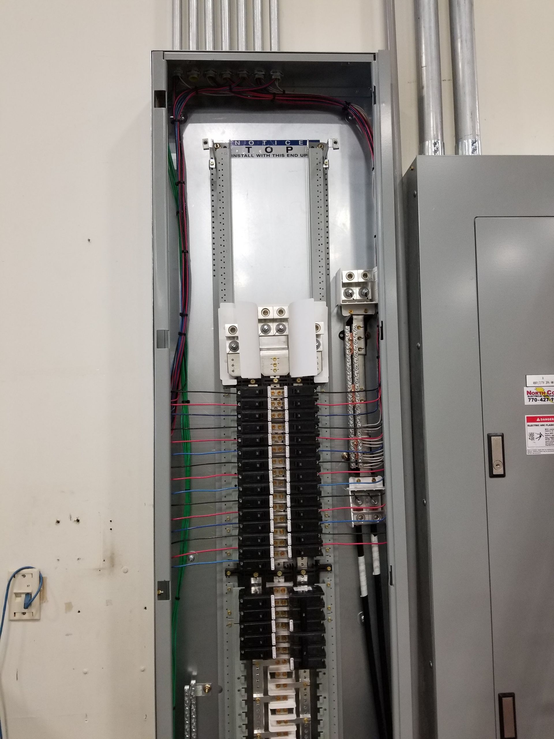 Electrical panel open, showing wiring and circuit breakers, mounted on a wall.