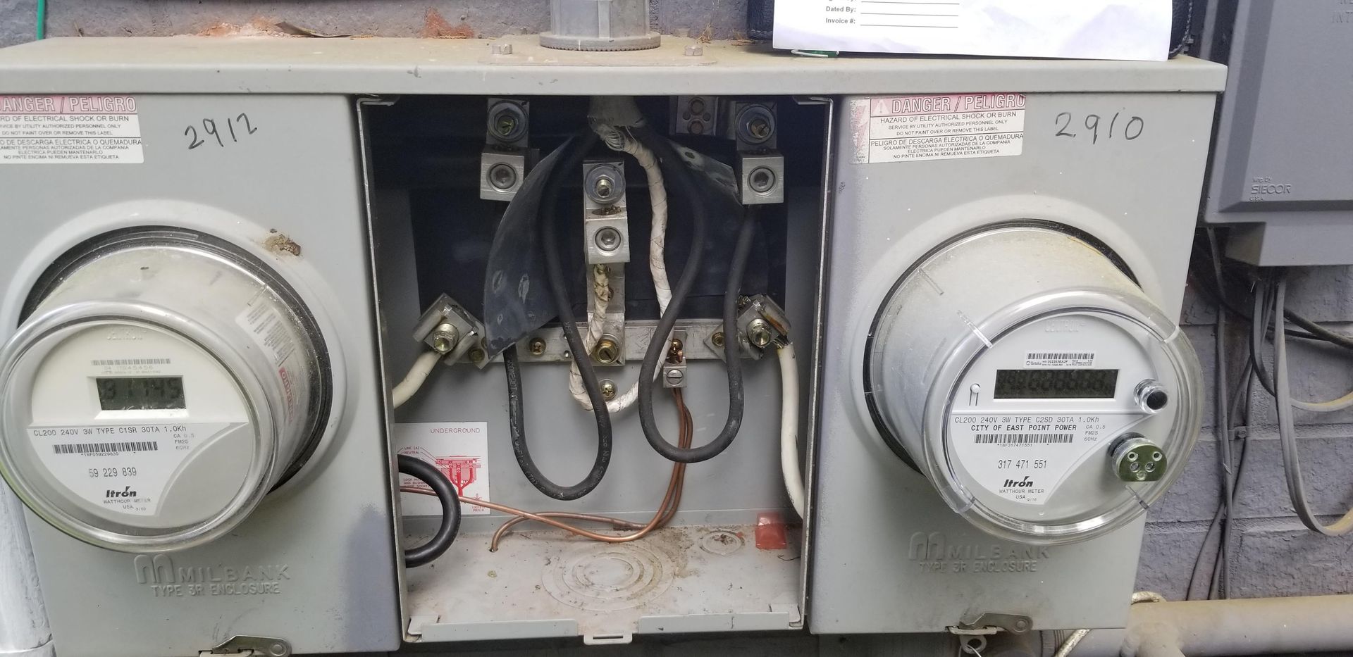 Electrical meter box with two meters and exposed wiring.