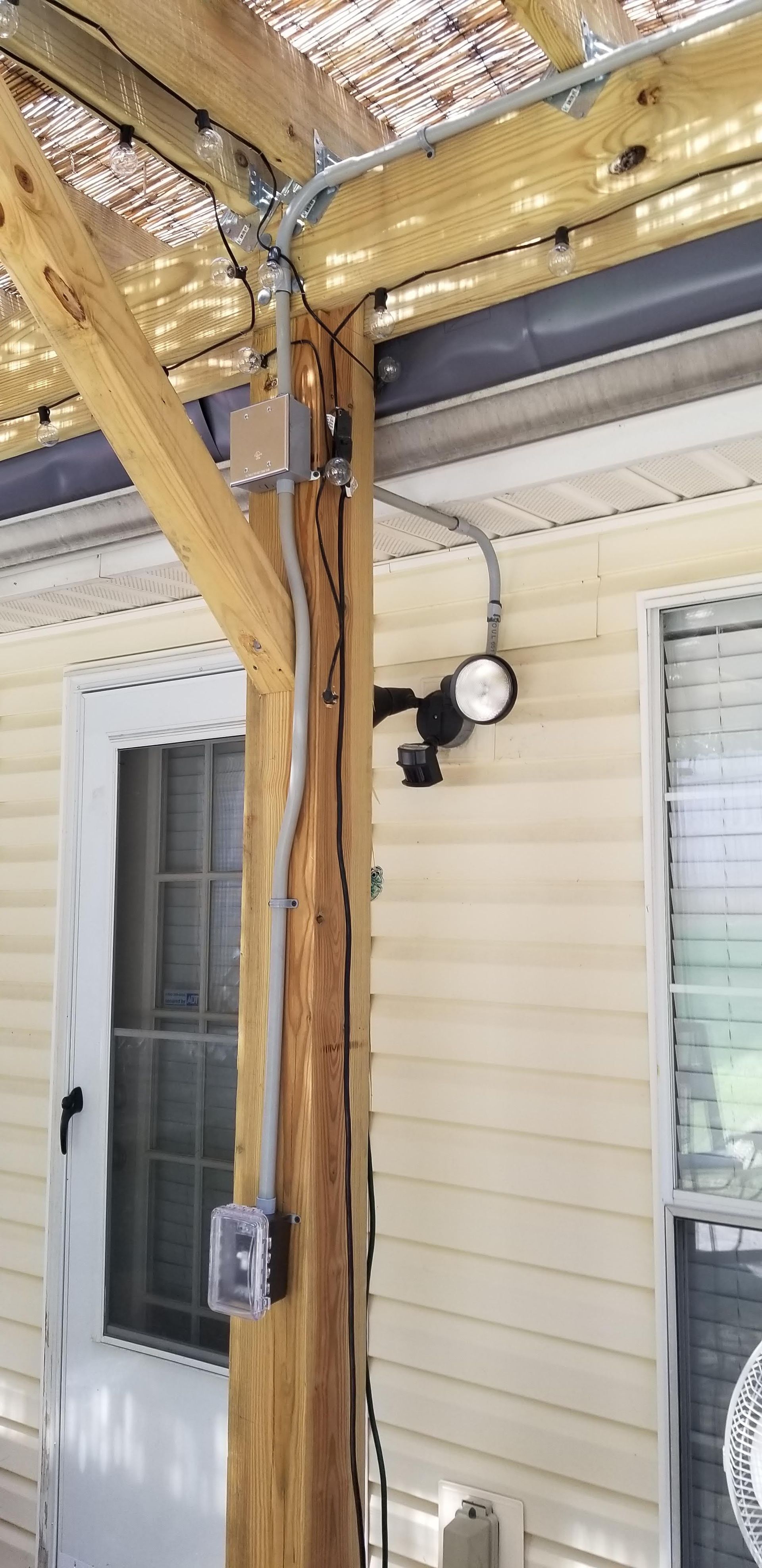 Electrical wiring and light fixture on a wooden post beside a door, outdoor setting.