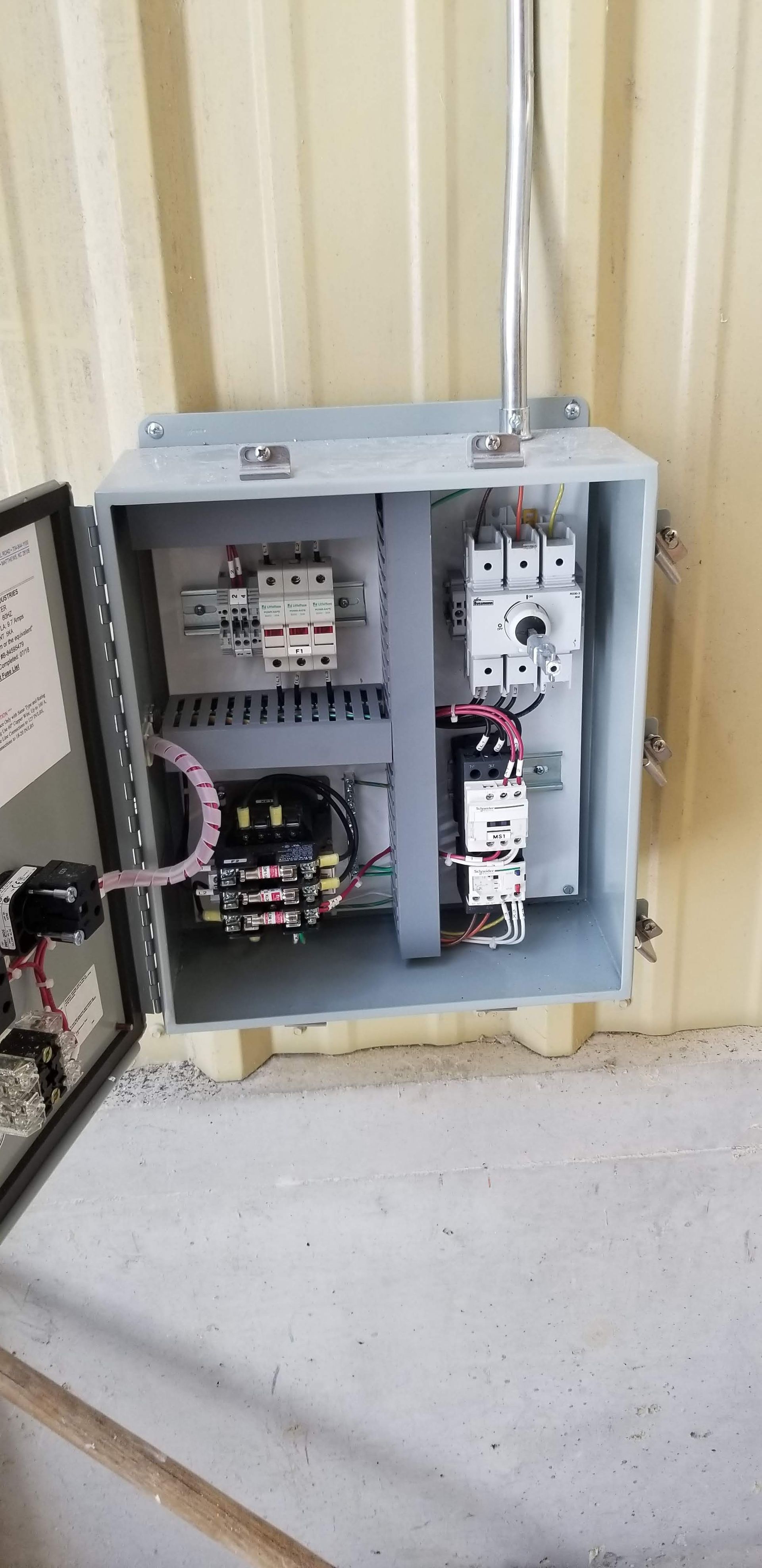 Open electrical panel on a wall. It has circuit breakers and wiring inside.