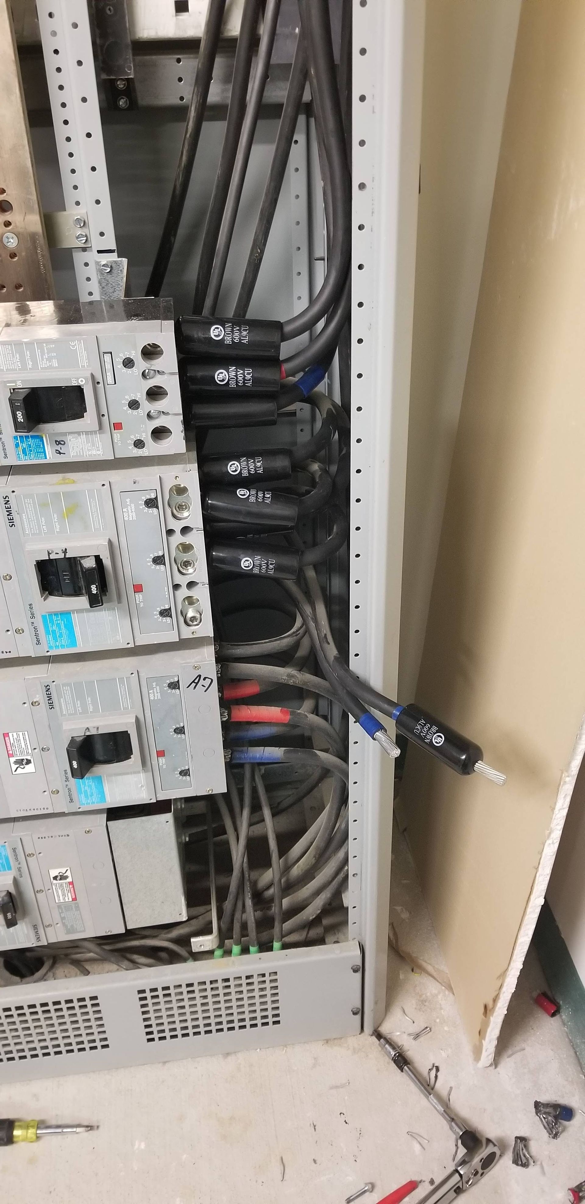 Electrical panel with cables and breakers, tools on floor.