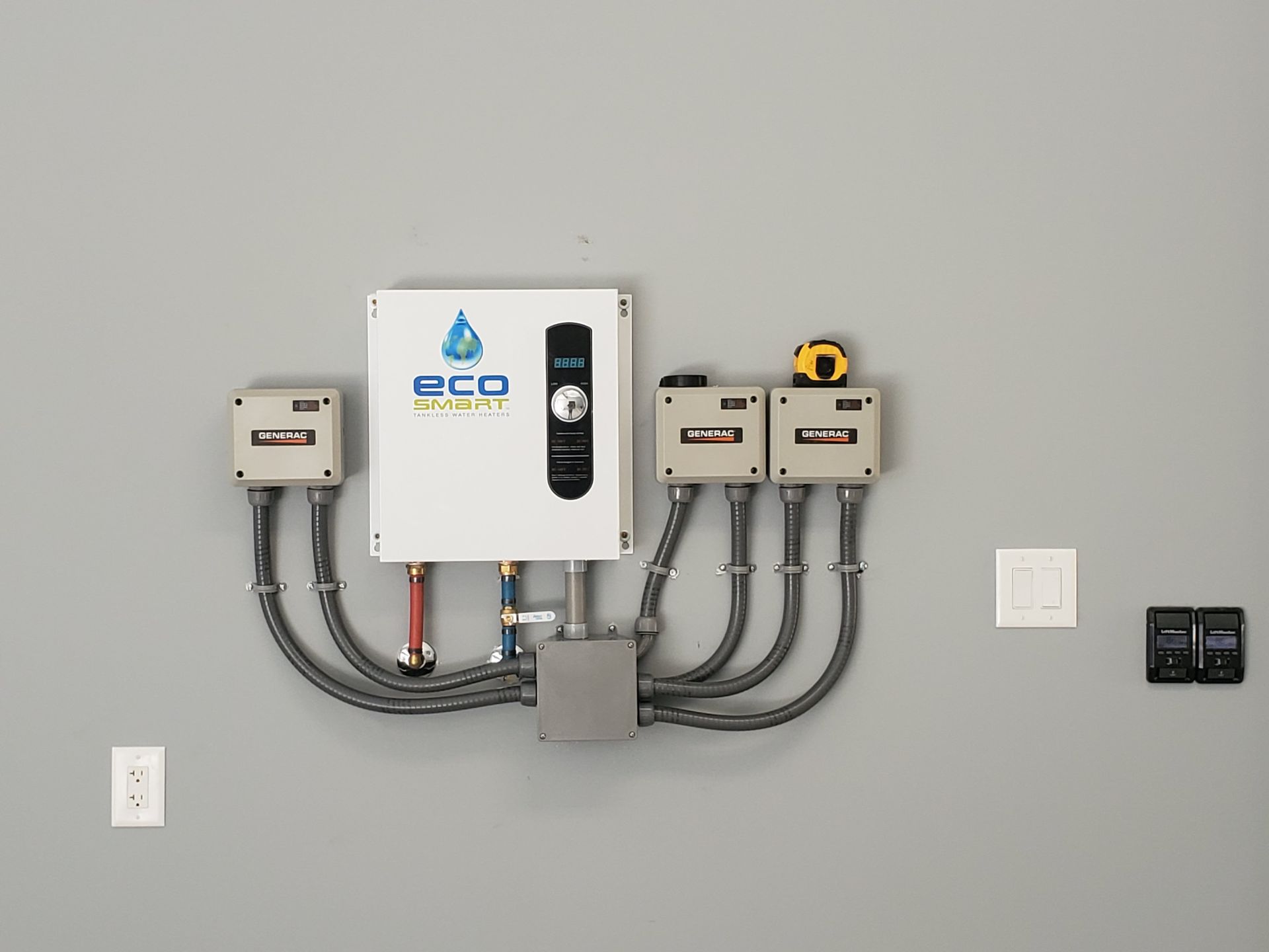 White EcoSmart water heater with black conduit and gray boxes mounted on a gray wall.