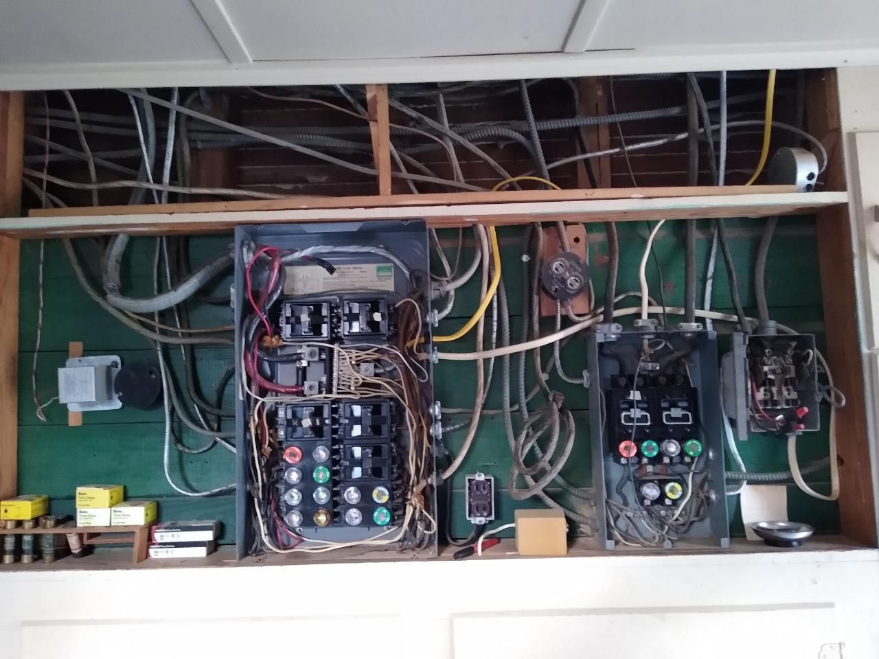 Electrical panels with exposed wiring in a wooden enclosure. Wires are gray, black, and yellow.