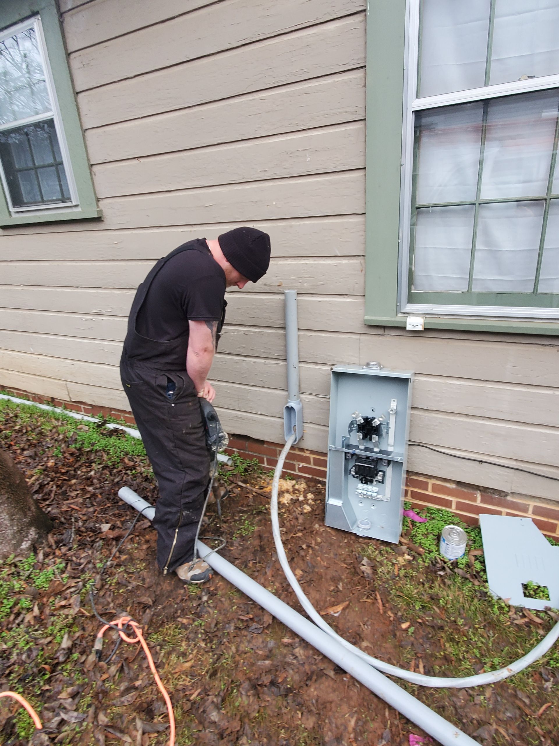Person working on electrical box on the side of a house.