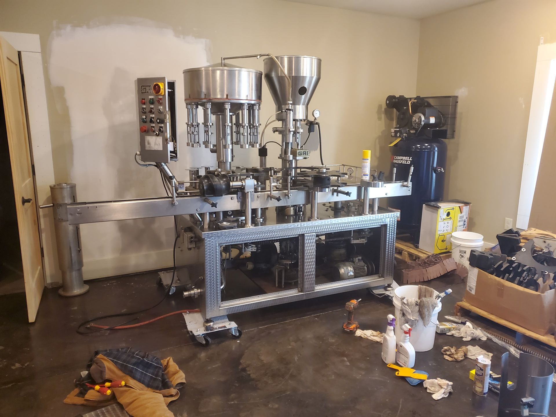 An industrial bottle filling machine in a room. Stainless steel, silver, and grey components.