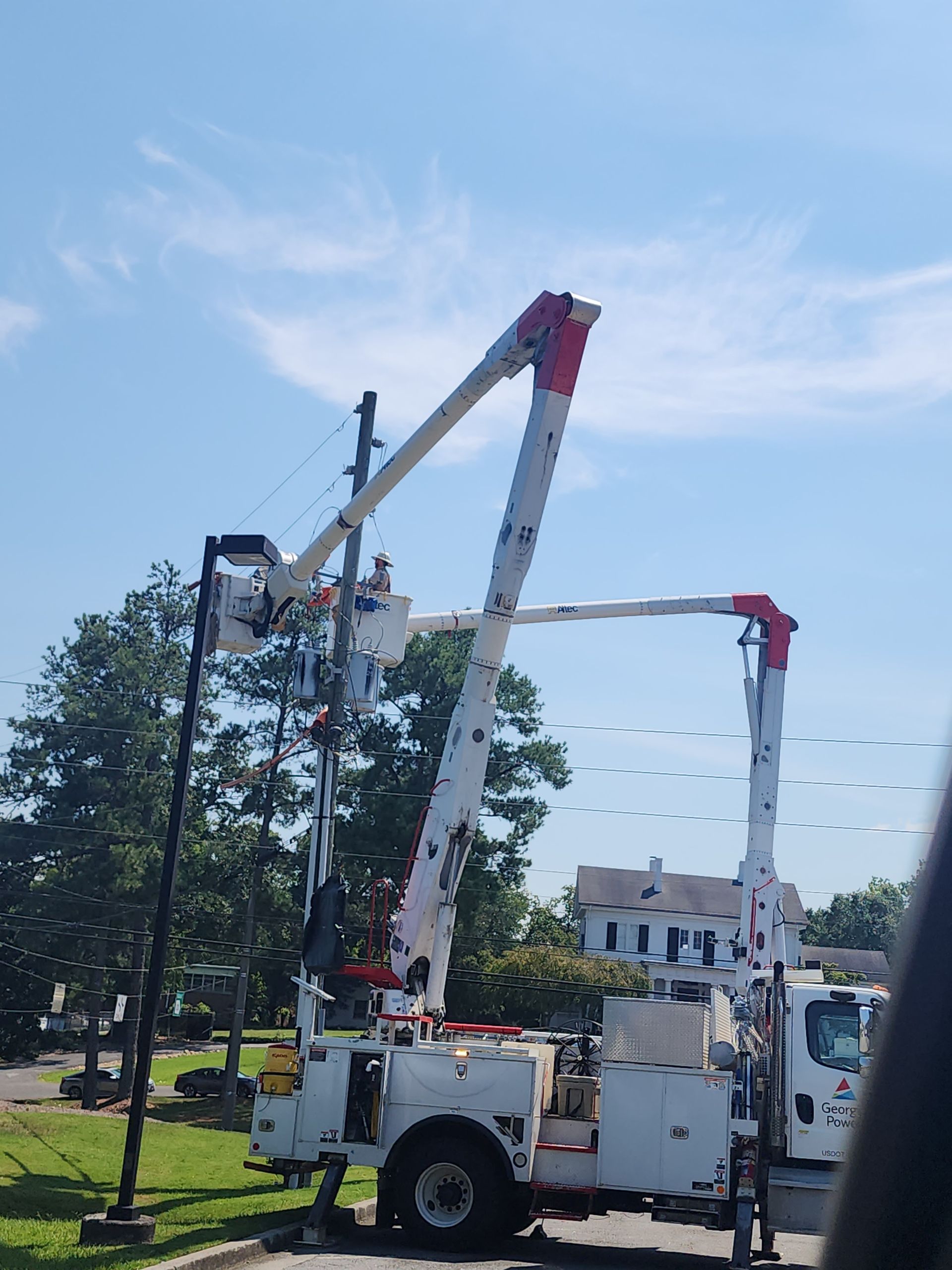 Utility truck with raised boom working on power lines against a blue sky.