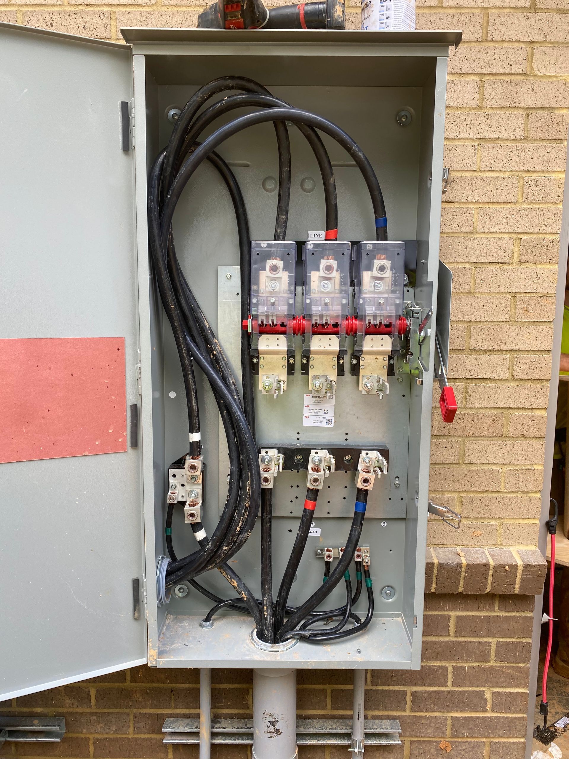Open electrical panel with black cables and circuit breakers on a brick wall.