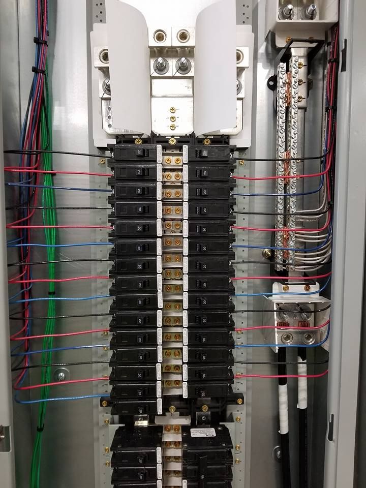 Electrical panel with rows of black circuit breakers and colored wires.