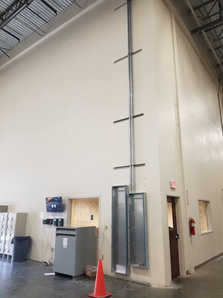 Tall, beige interior wall with metal electrical conduit. Electrical panels on wall. Red cone and door.
