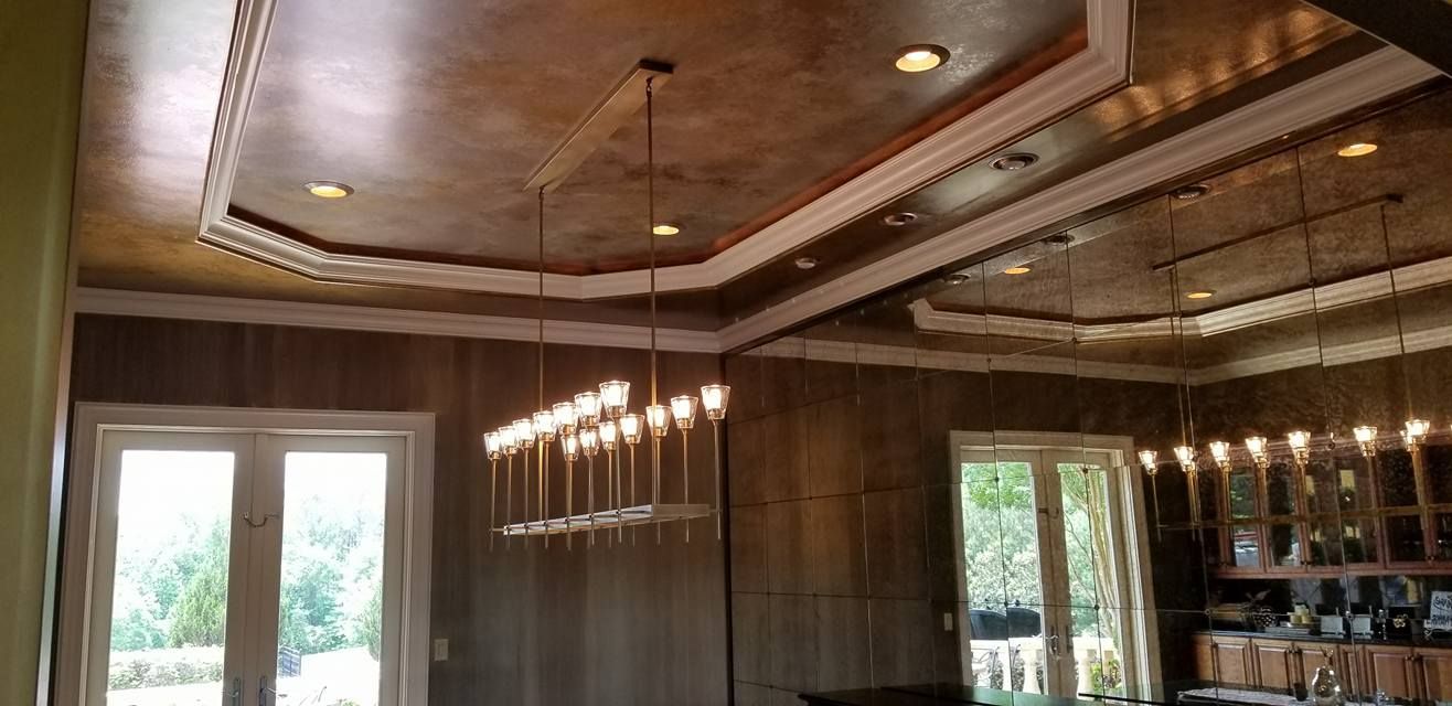 Interior view of a room with a decorative ceiling, chandelier, and windows overlooking greenery.