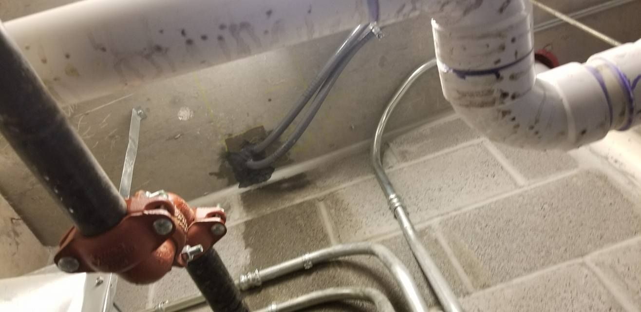Pipes and conduits run along a concrete ceiling with a red pipe fitting.