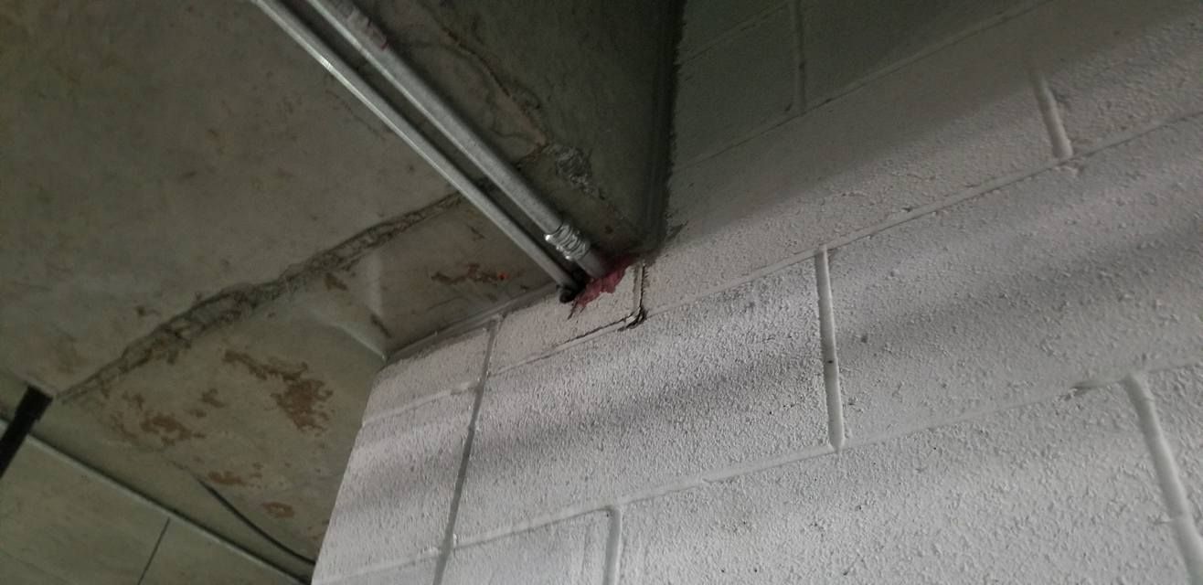 Concrete block wall with a conduit running along the top corner, a crack appears on the right.