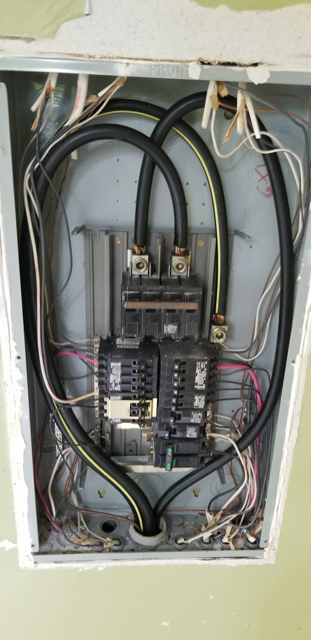 Electrical panel with exposed wiring. Black cables loop around circuit breakers.