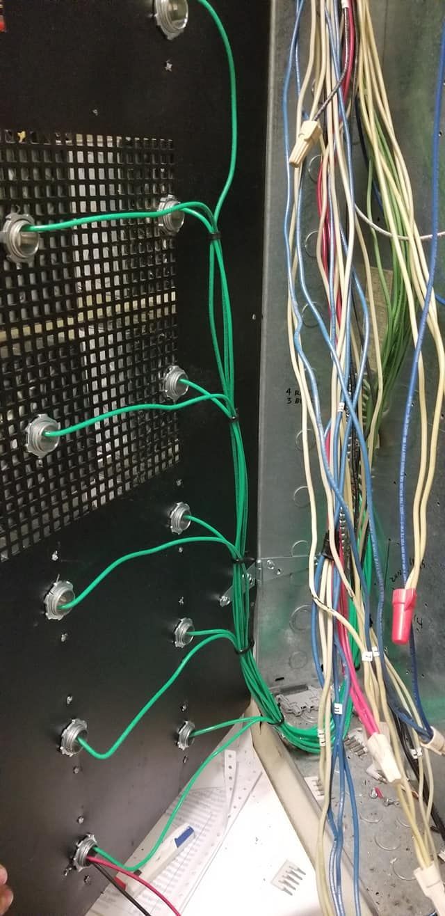 Inside of a panel, a network of green and multicolored wires are connected.