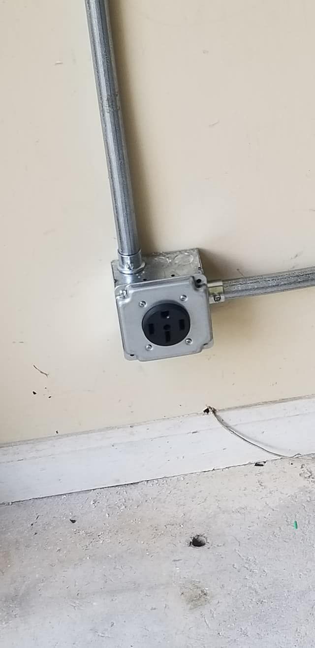 Electrical outlet with conduit on a tan wall, near a dirty white baseboard.