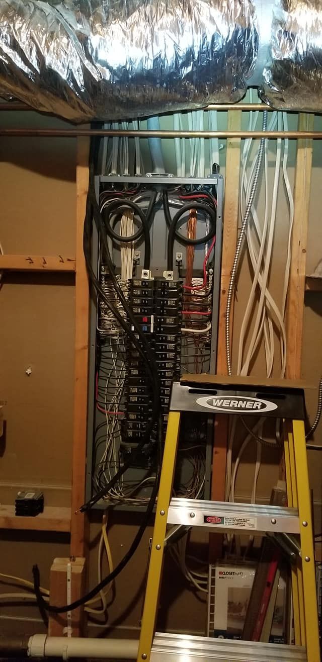 Electrical panel with wiring, yellow ladder, and silver ductwork in a basement setting.