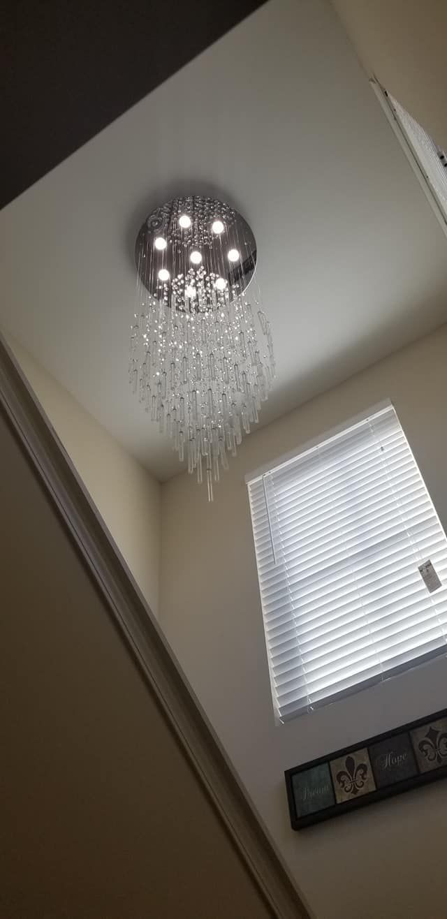 A ceiling-mounted chandelier with crystal beads, near a window with blinds.