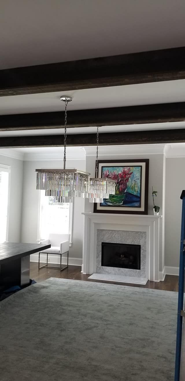 Living room with fireplace, rug, and crystal chandeliers under dark wood beams.