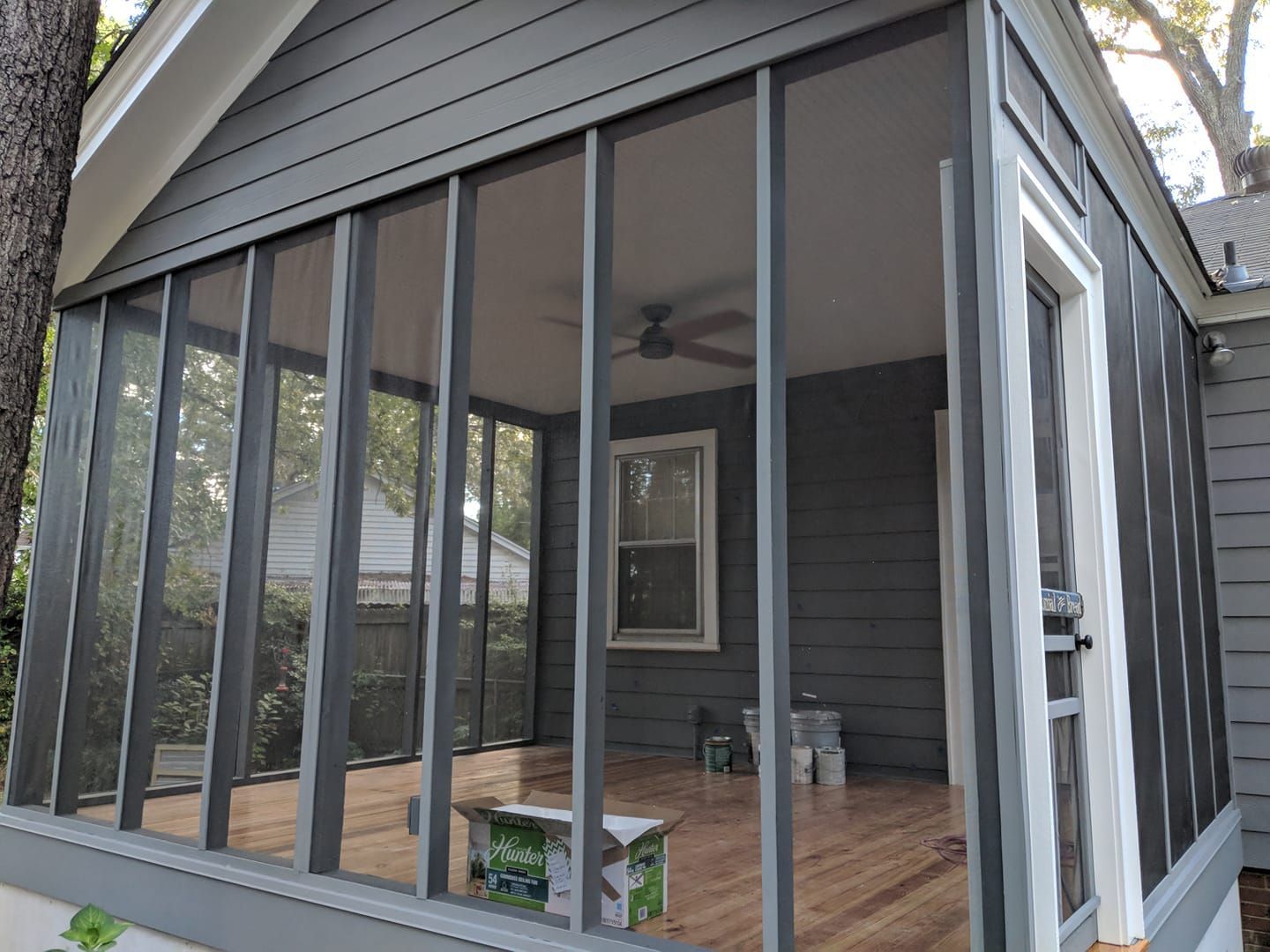 Screened-in porch with gray siding and wooden floor. A window and ceiling fan are visible inside.