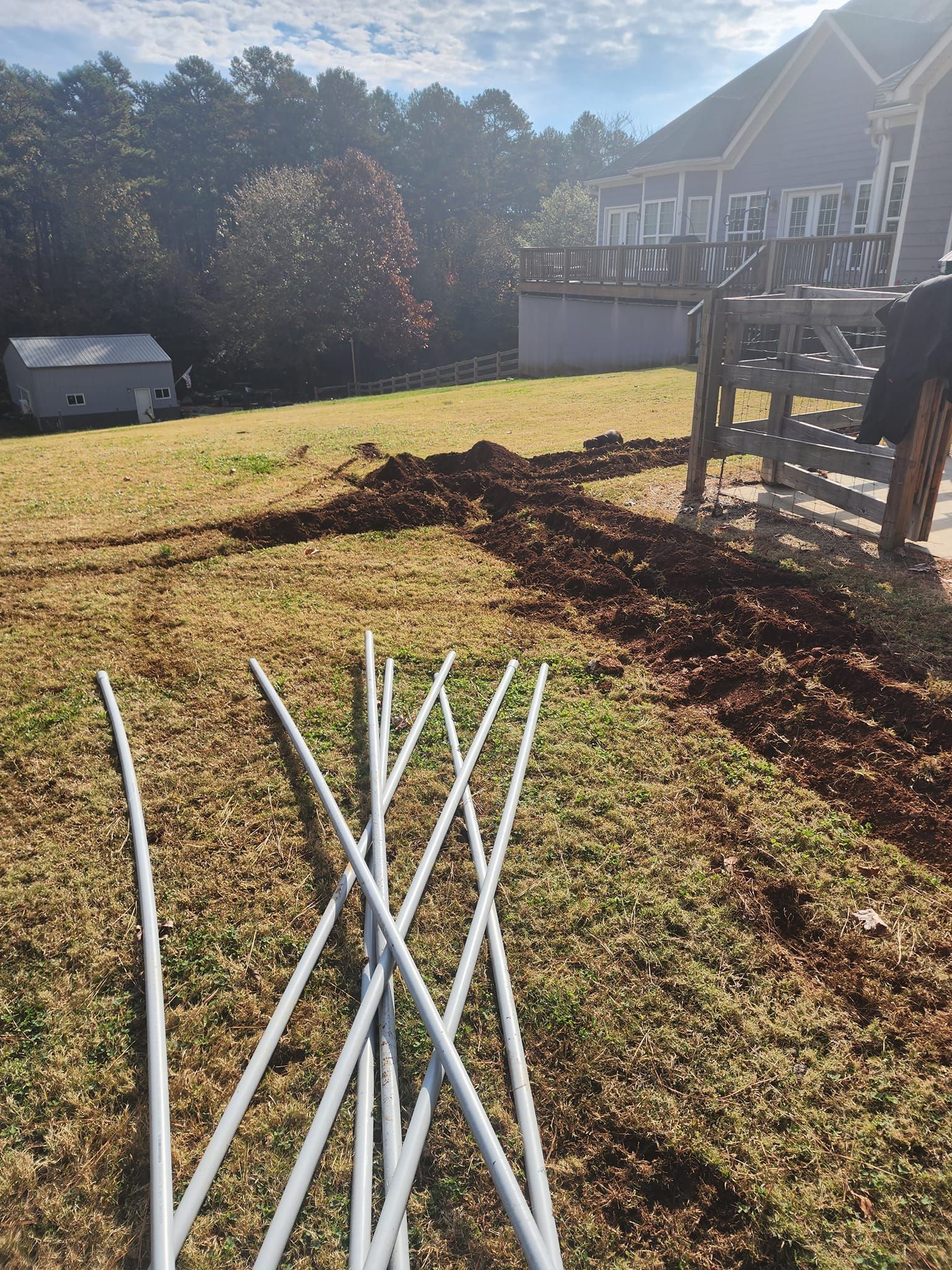 Gray poles on a grassy yard, dirt path leading to a deck and shed, sunny day.