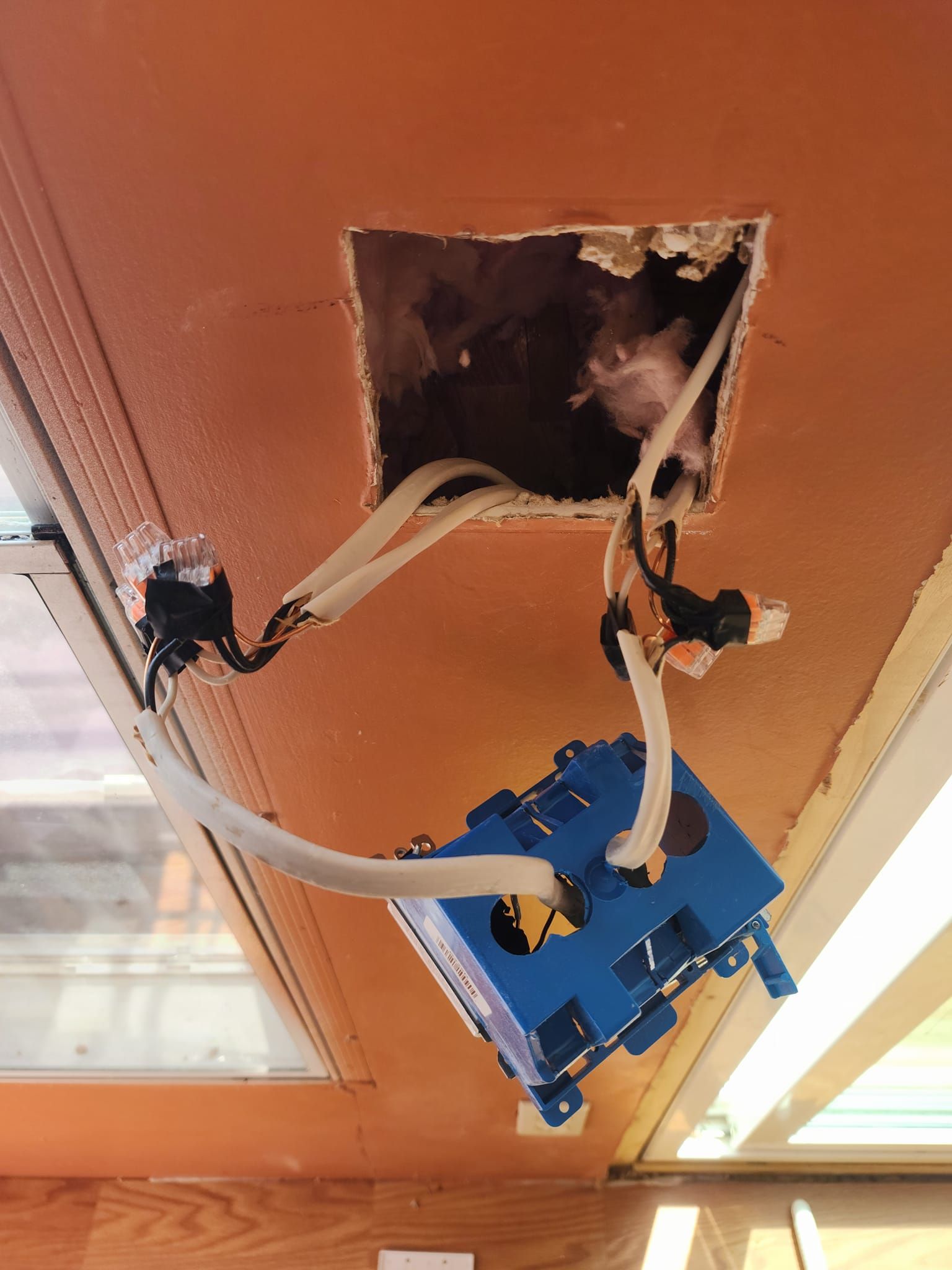 Ceiling electrical wires and blue junction box within a ceiling opening.