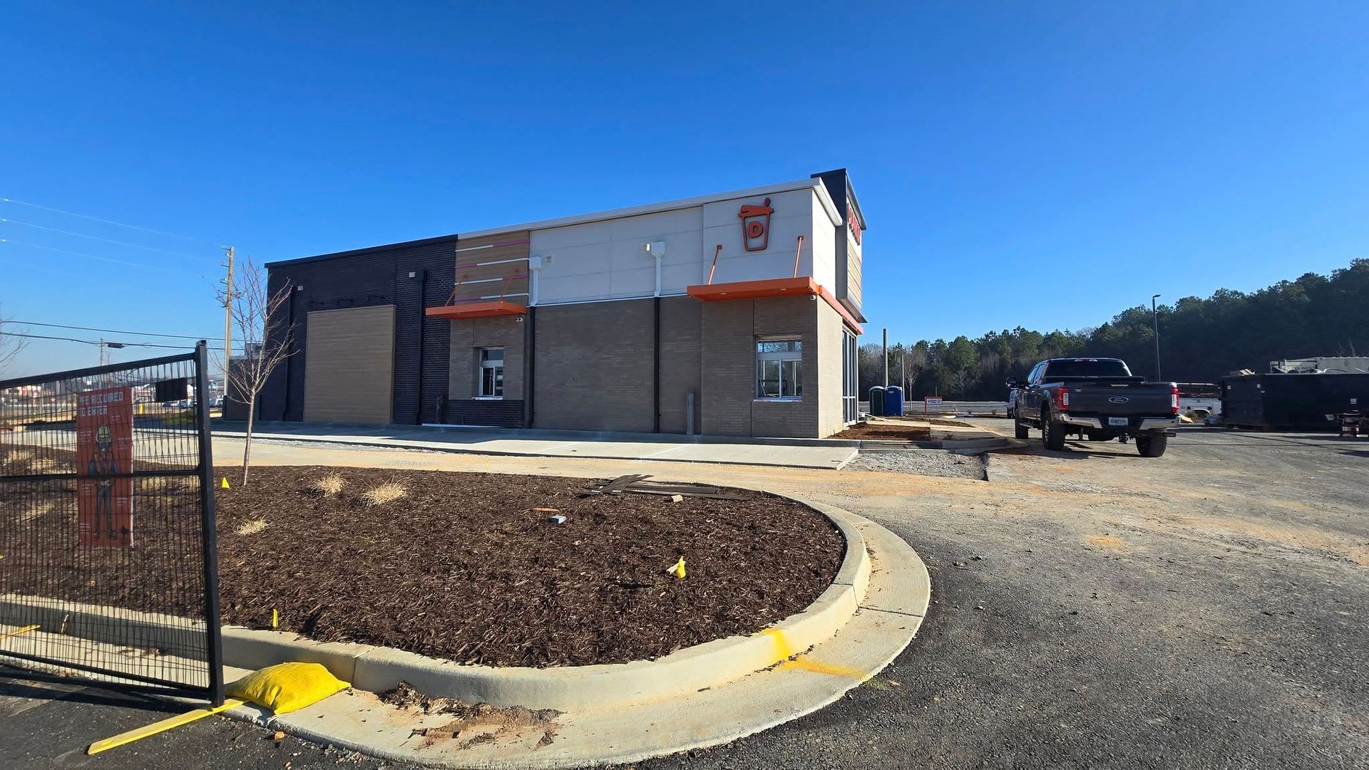 Construction site with a partially built, brick and light-colored building under a clear blue sky. A truck is parked nearby.