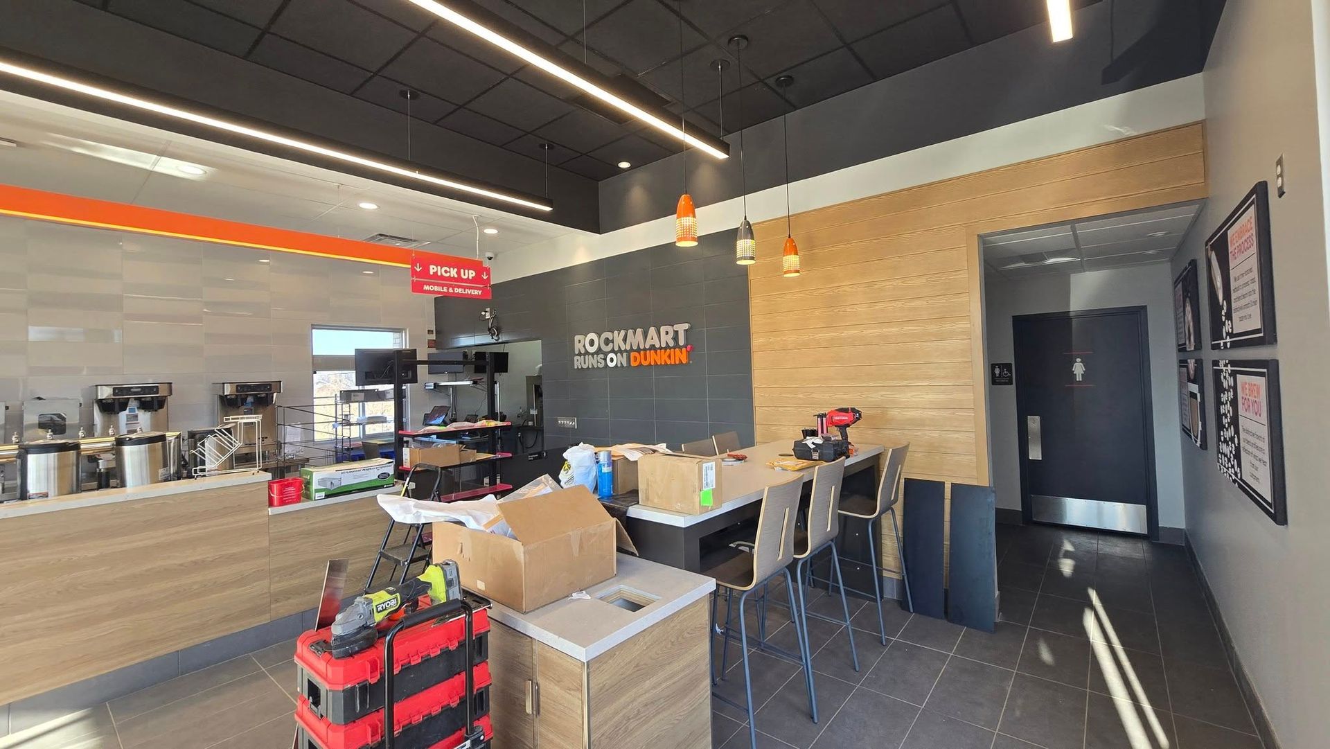 Interior of a restaurant under construction, with tables, counters, boxes, and tools.
