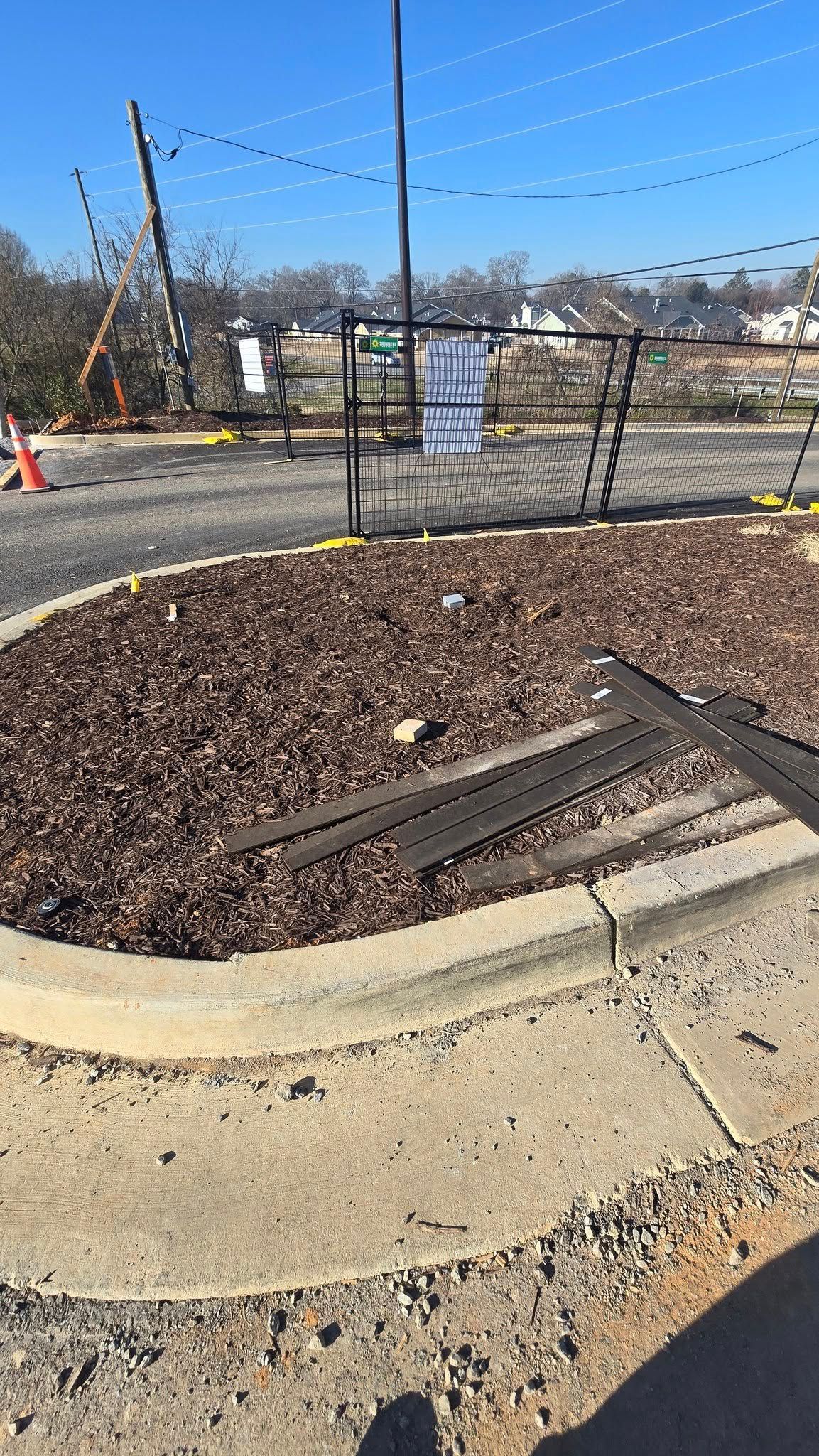 A landscaped bed filled with mulch is bordered by a concrete curb. A black fence surrounds the bed.