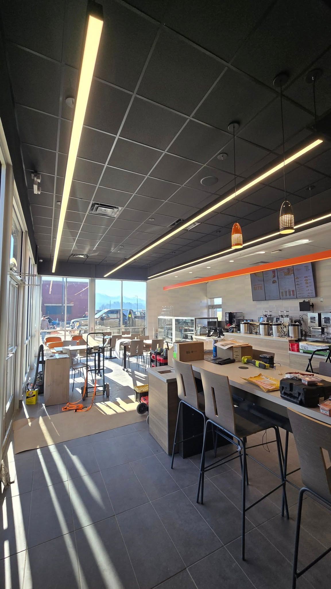 Bright, modern interior with linear lights. Tables and stools are in front of a counter with, construction still ongoing.