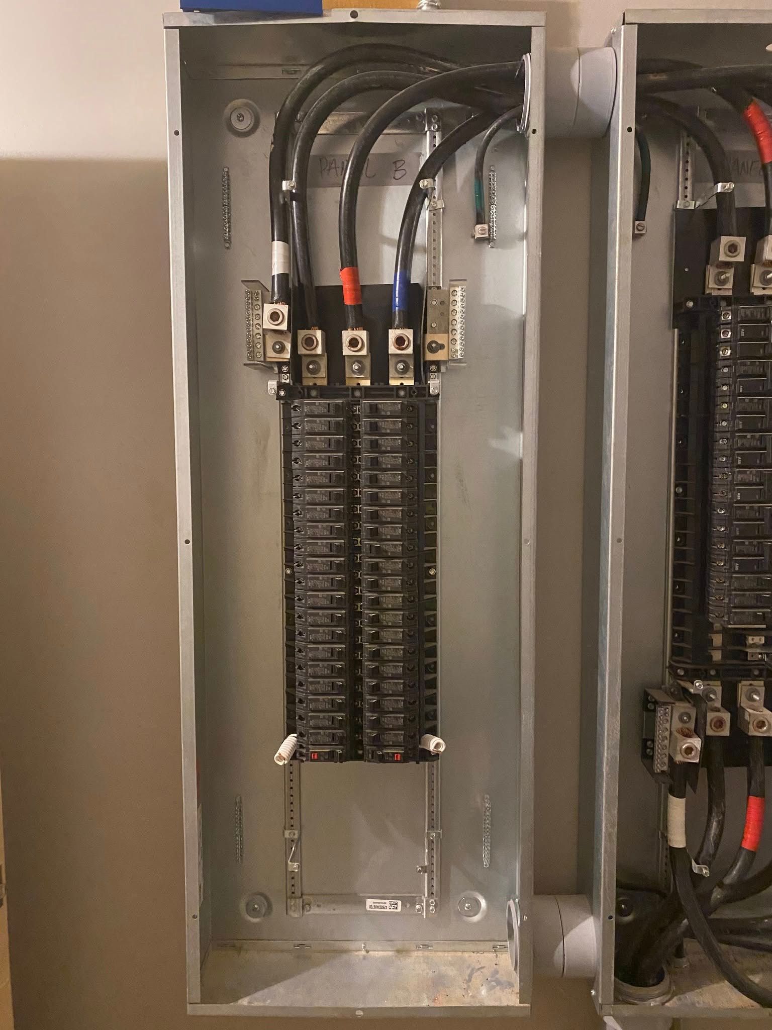 Electrical panel with black wires, circuit breakers, and connection points inside a metal cabinet.