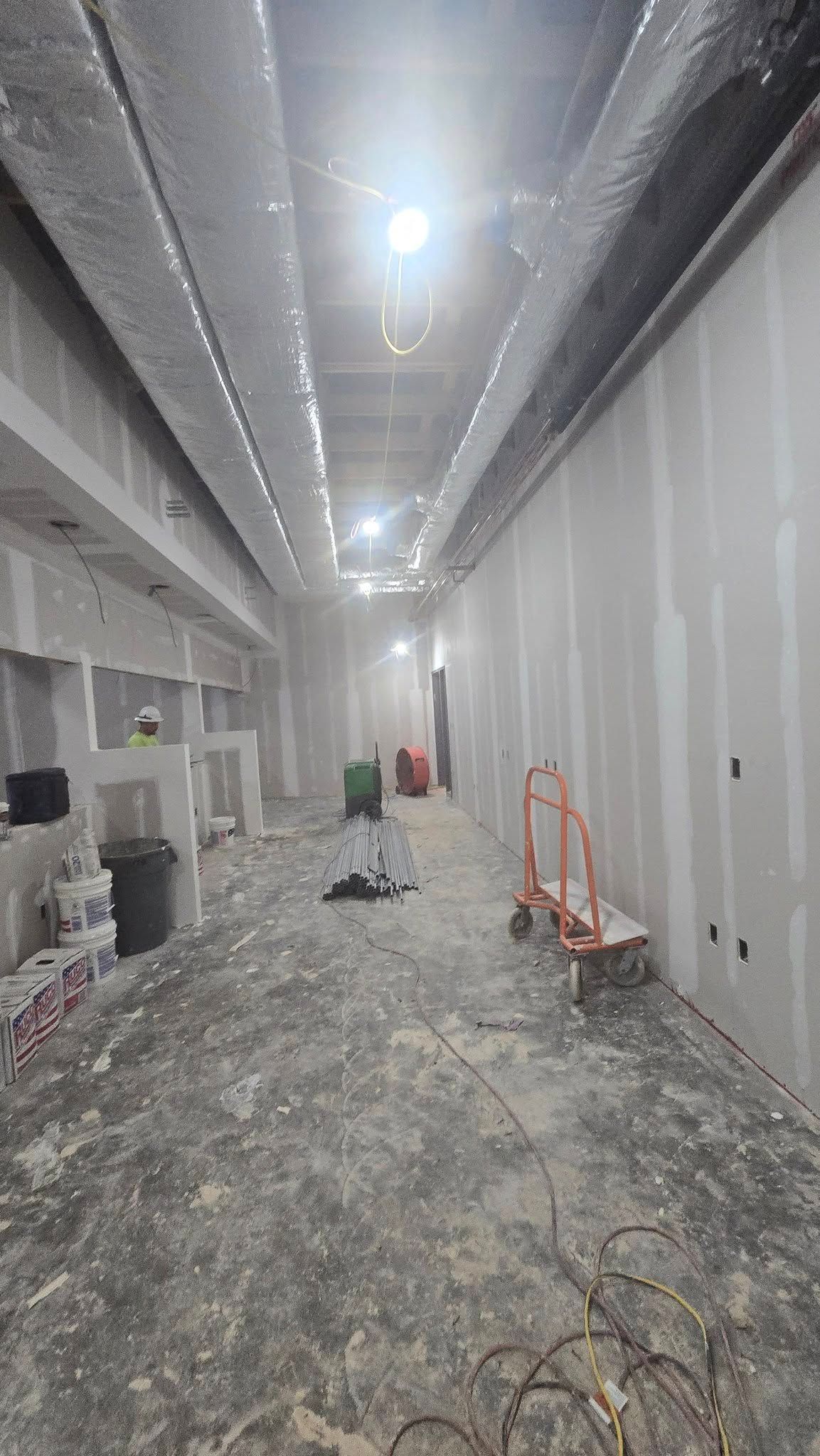 Interior construction site: long hallway with drywall, ductwork, and equipment.