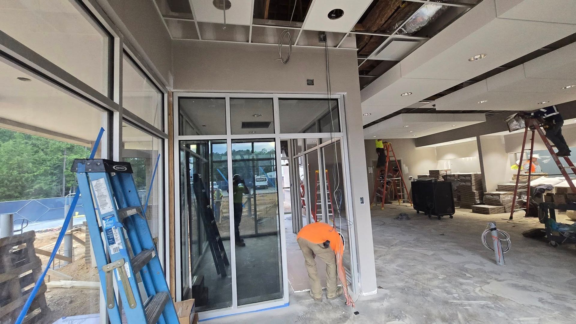 Construction site: Workers inside a building with incomplete ceilings, walls, and flooring. Ladders and tools are present.