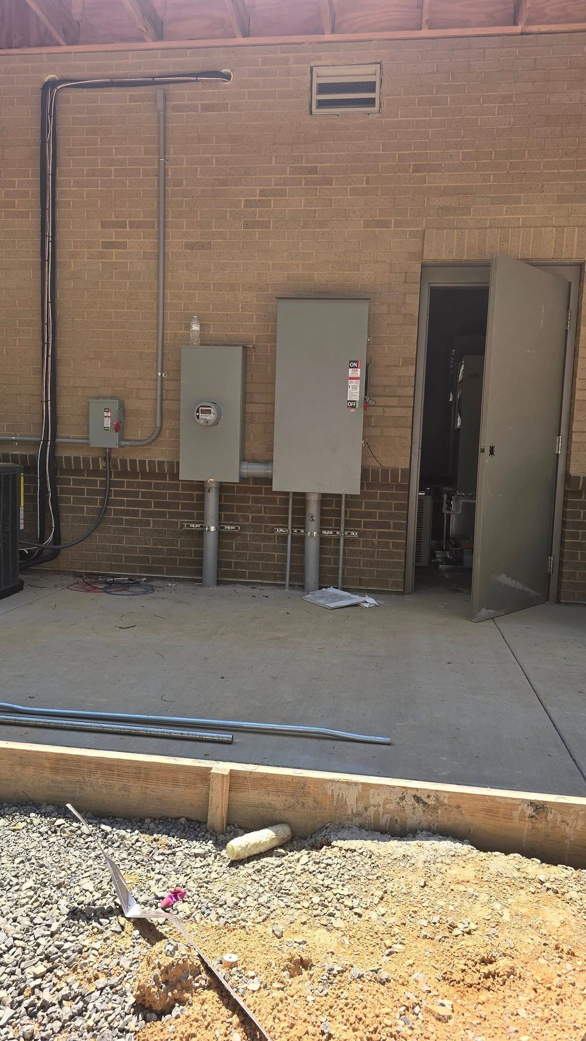 Brick wall with electrical boxes, open door to a room, conduit, and gravel border.