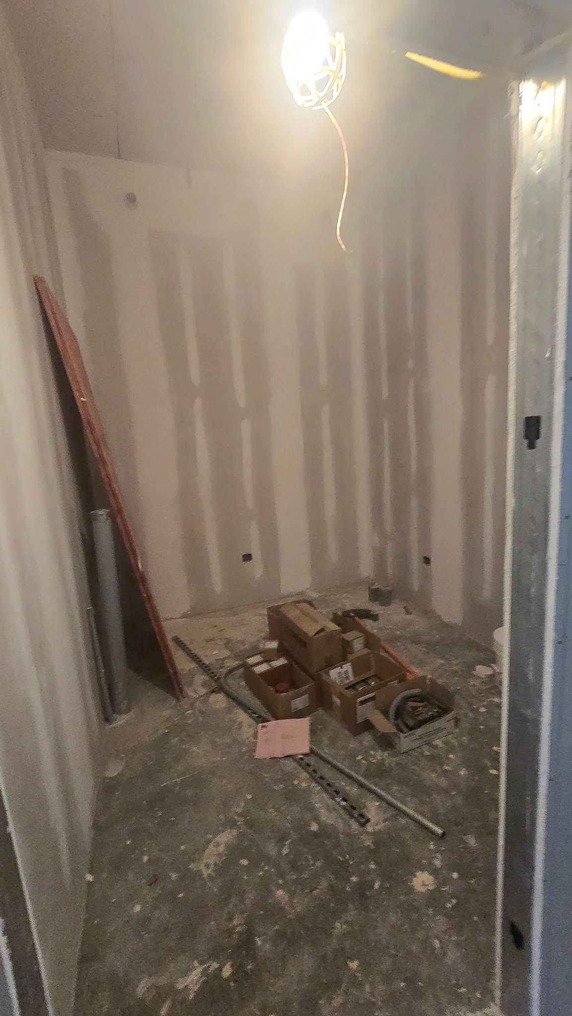 Construction site interior with tools, drywall, and a dangling light.