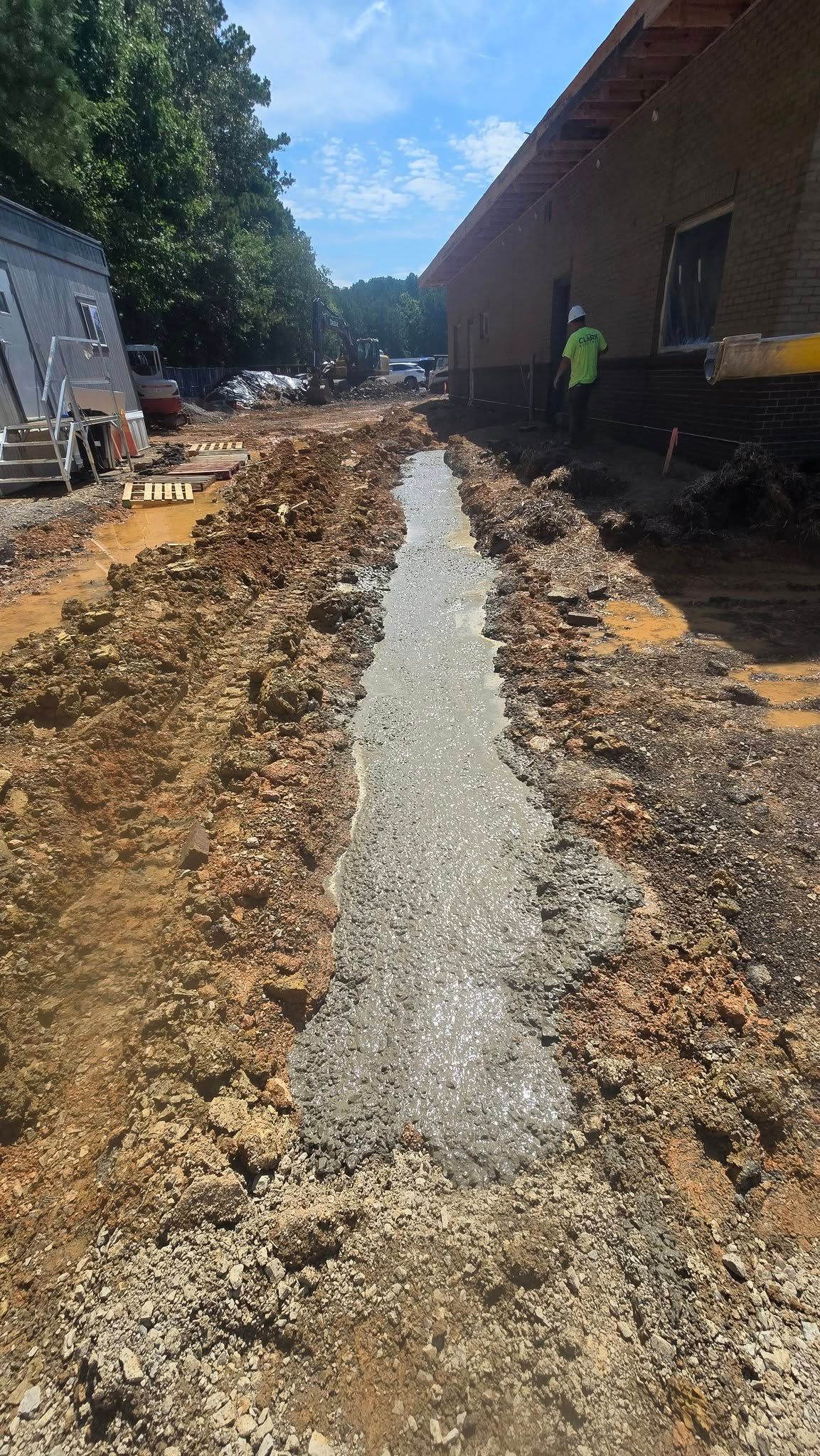 Construction site with a concrete trench running between dirt and a building.
