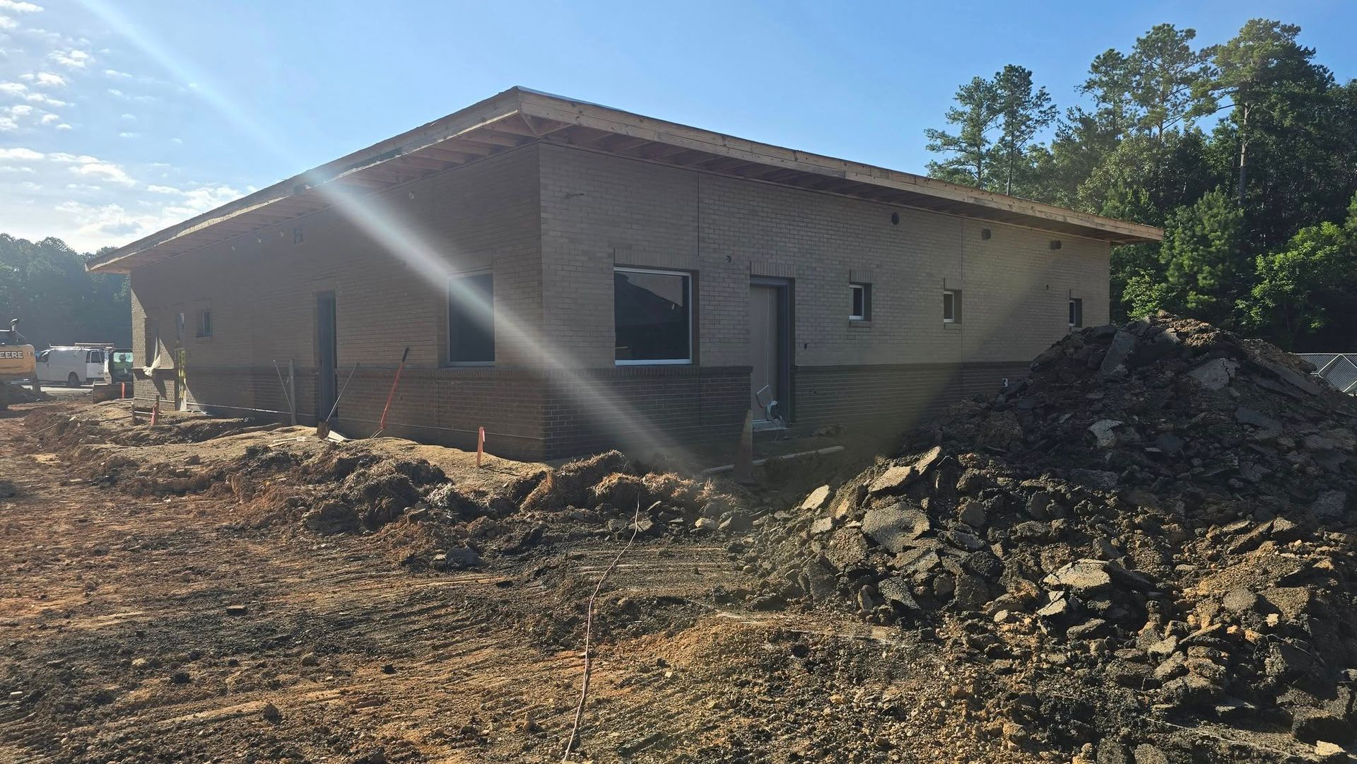 Building under construction with dirt pile in front. Brown siding, windows, and exposed wood roof.