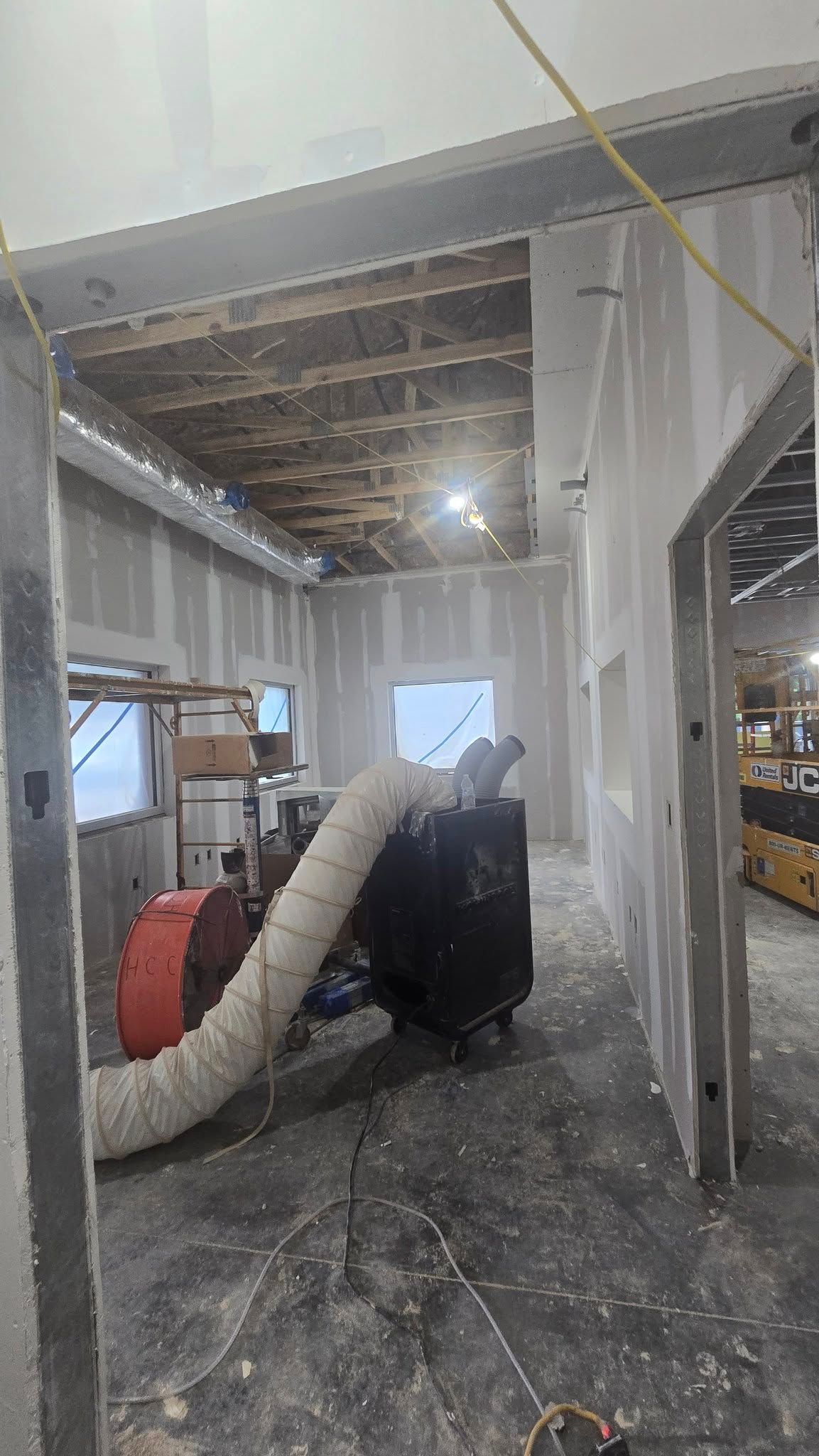 Interior construction, drywall walls, ceiling framework exposed. A large air filtration unit with flexible ducting.